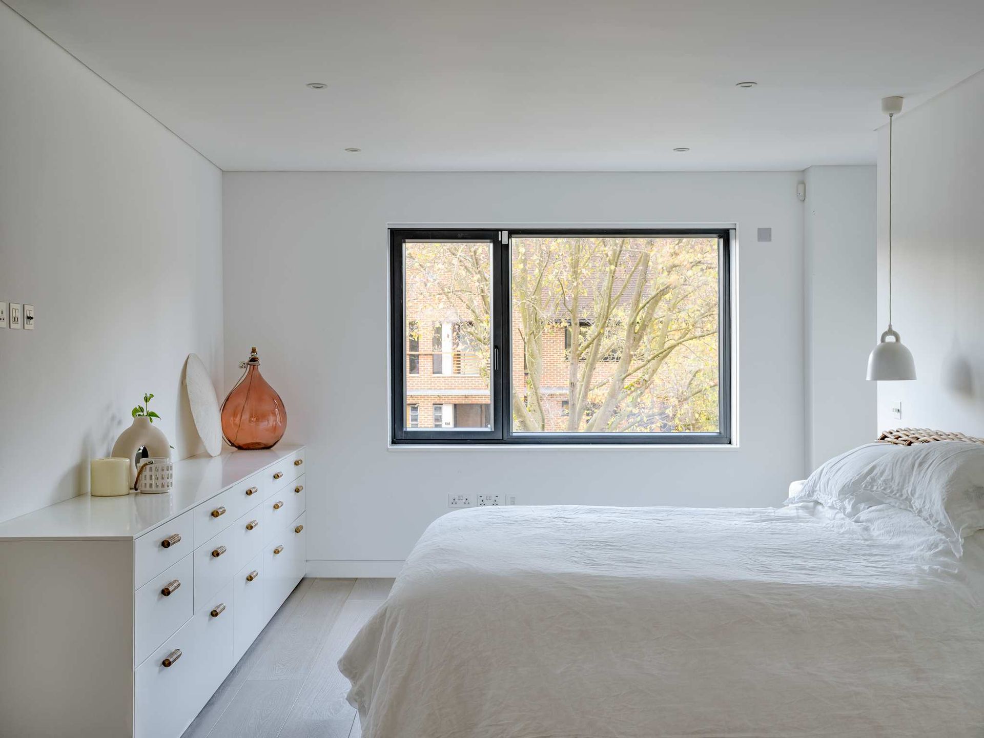Minimal white bedroom with a window, dresser, and bed.