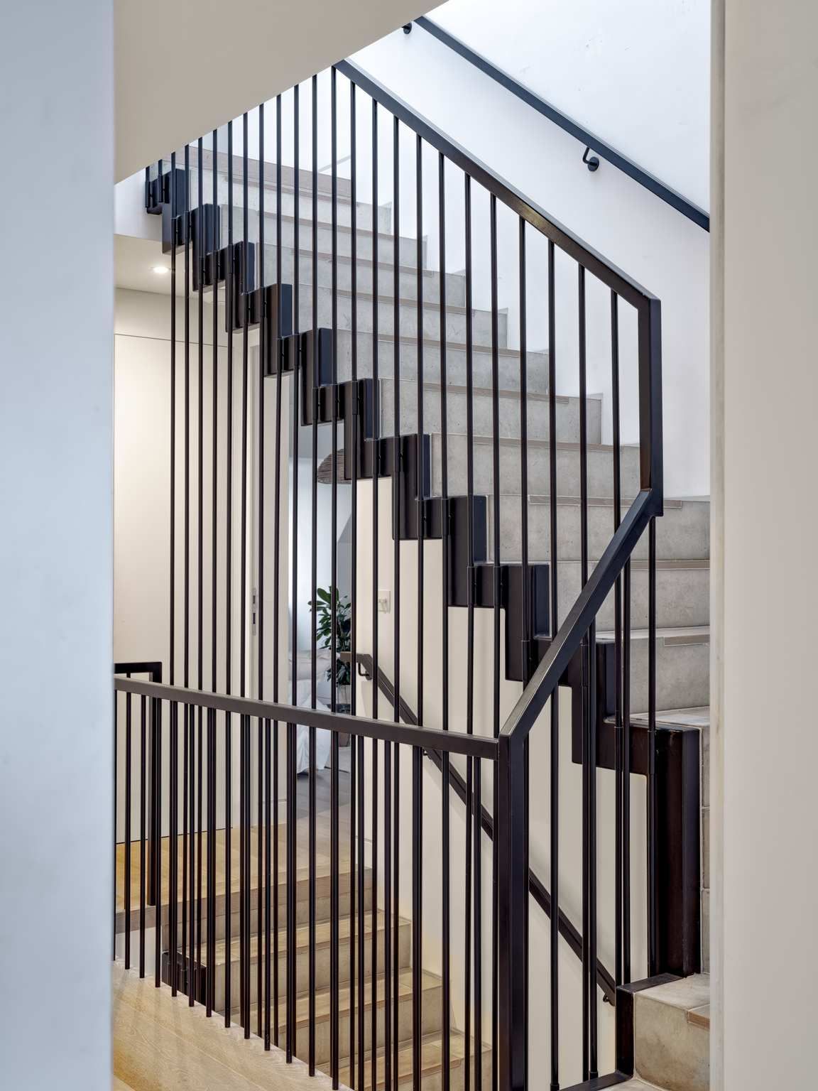 Modern staircase with black metal railing and glass panels in a bright interior.