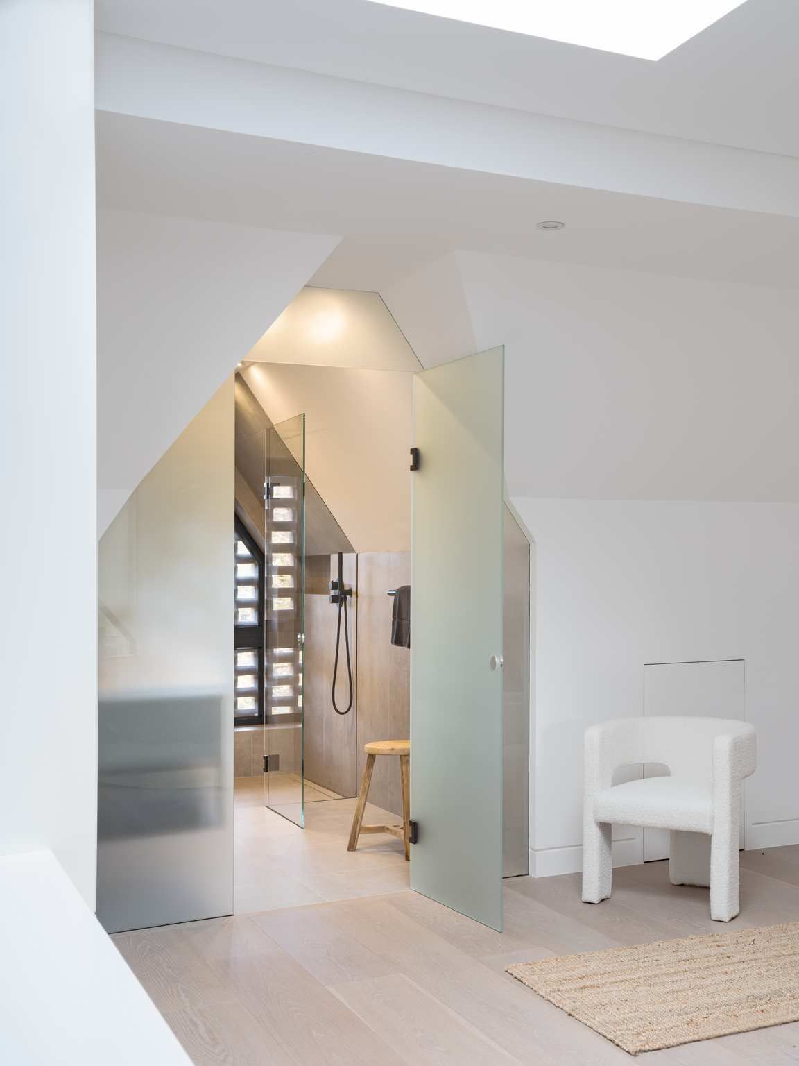 Modern bright hallway with geometric doorway, mirror, and a white chair on a rug.