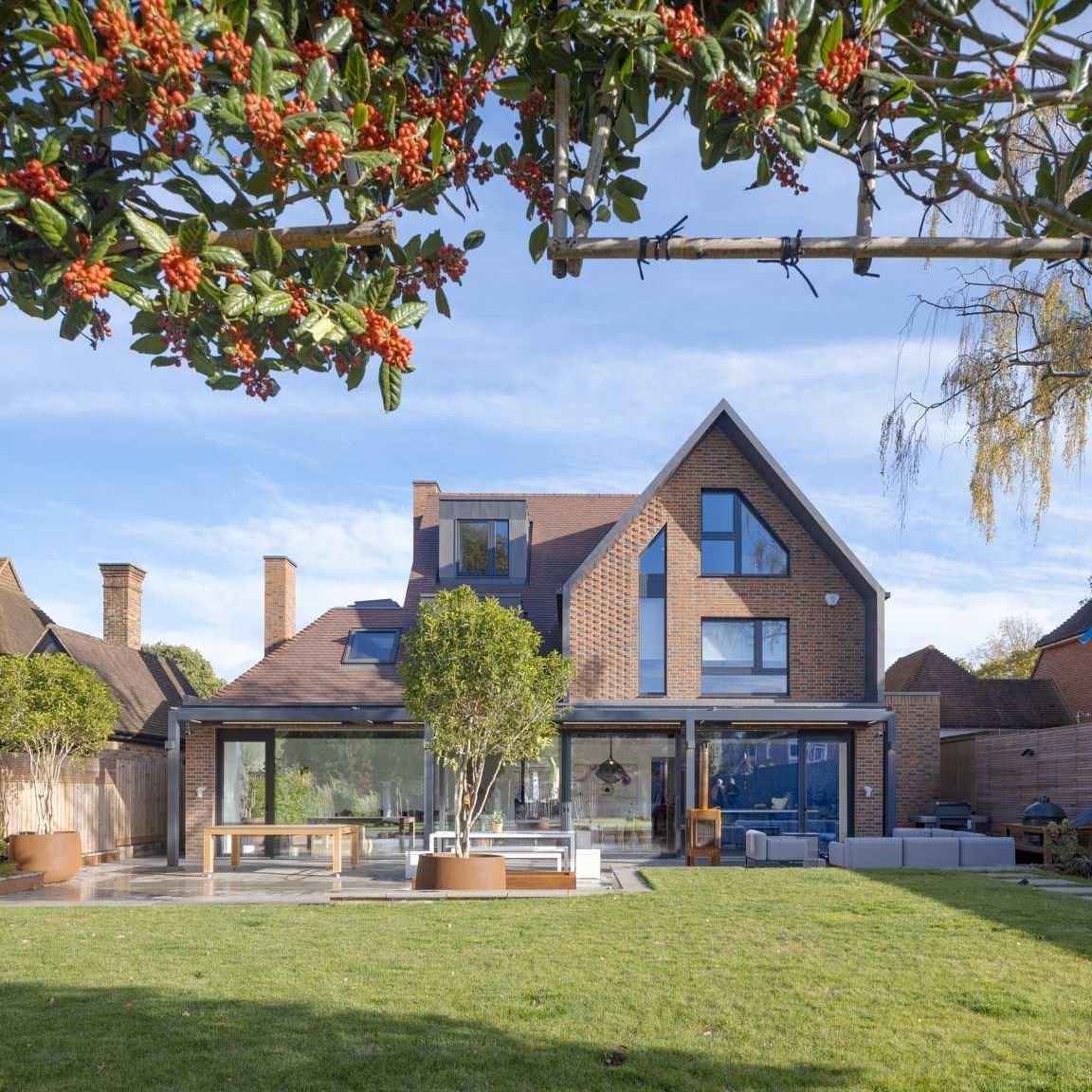 Modern brick house with large windows, patio, and green lawn under a blue sky
