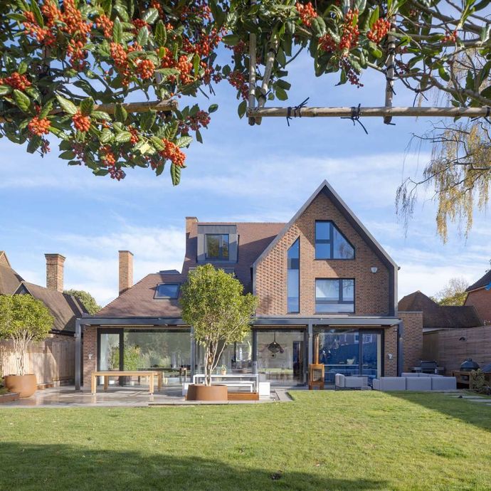 Modern brick house with large windows and a glass extension, viewed from a green lawn under a blue sky
