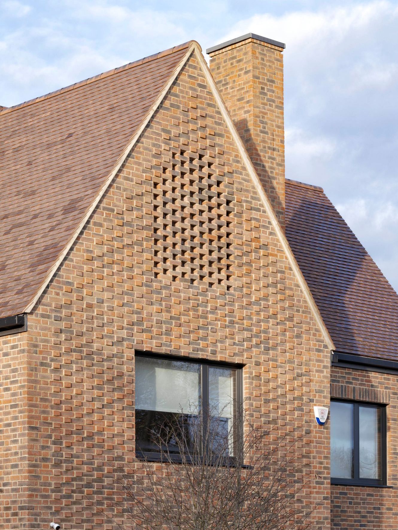 Brick house gable with diamond-pattern vents and windows under a tiled roof