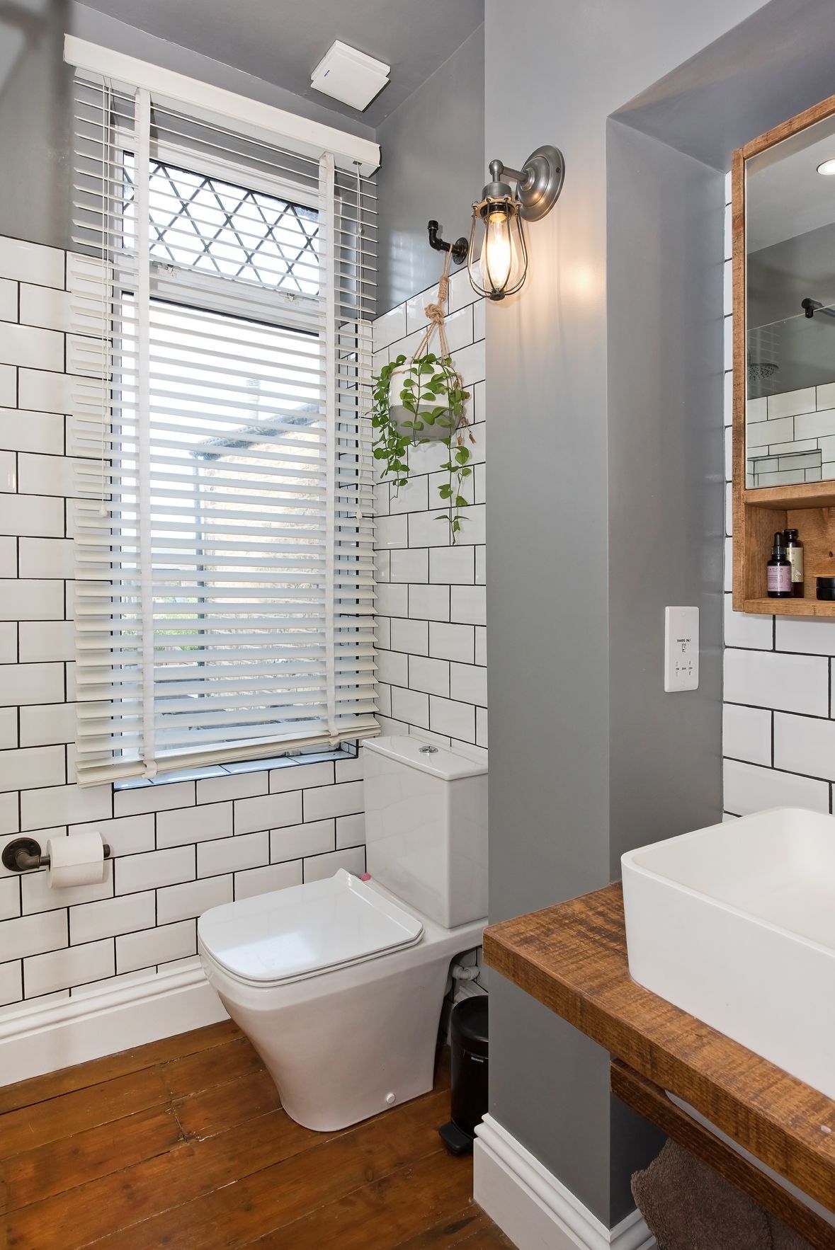 Small modern bathroom with white subway tile shower, toilet, window blind, and wood vanity.