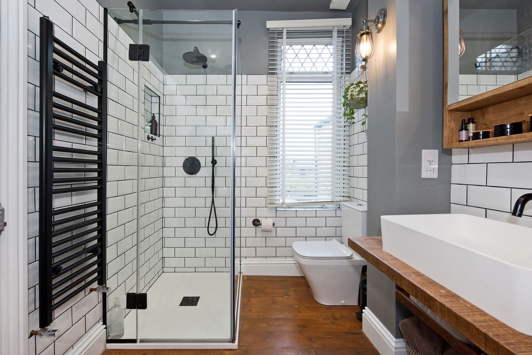 Modern bathroom with glass shower, black towel warmers, white tile, wood floor, and white sink vanity