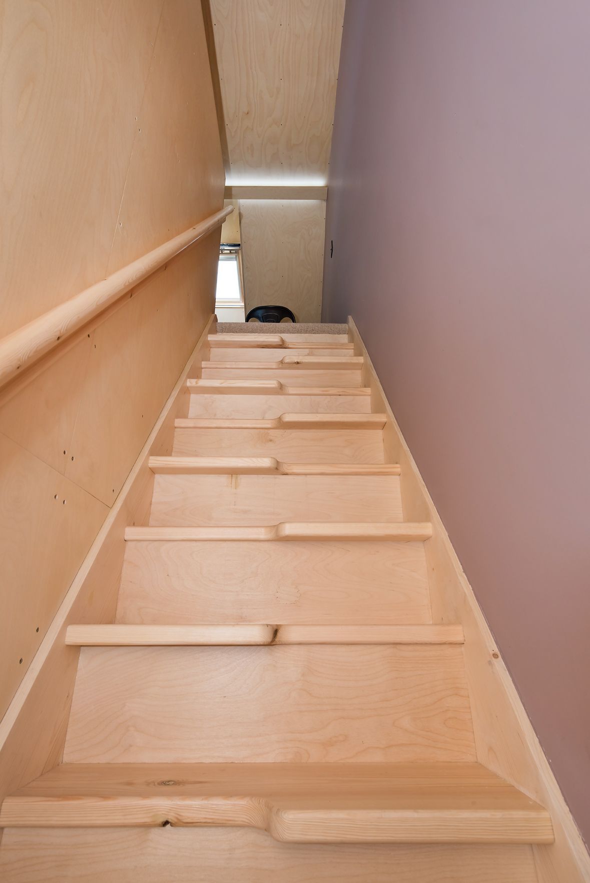 Wooden ladder leading up a narrow stairwell between beige and gray walls
