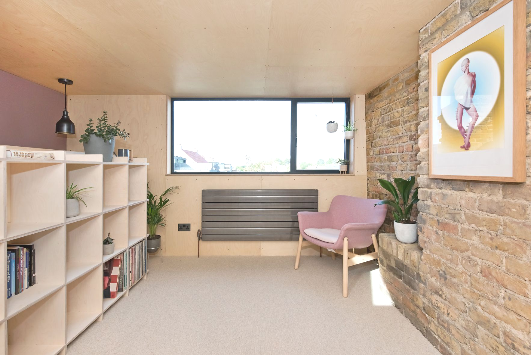 Bright cozy room with shelves, pink chair, stone wall art, and a large window.