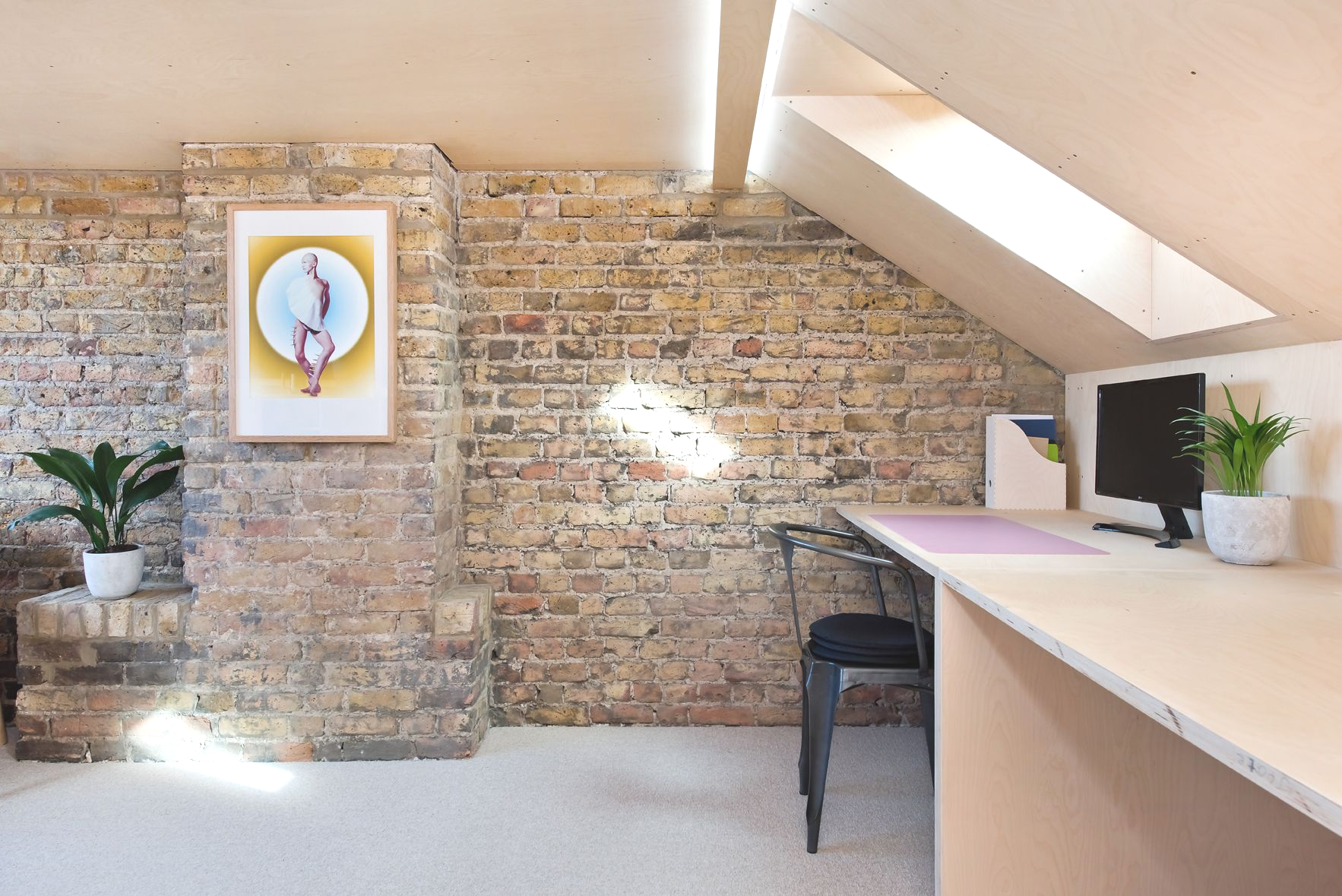 Bright office reception area with brick wall, framed art, plants, and a counter under a slanted ceiling