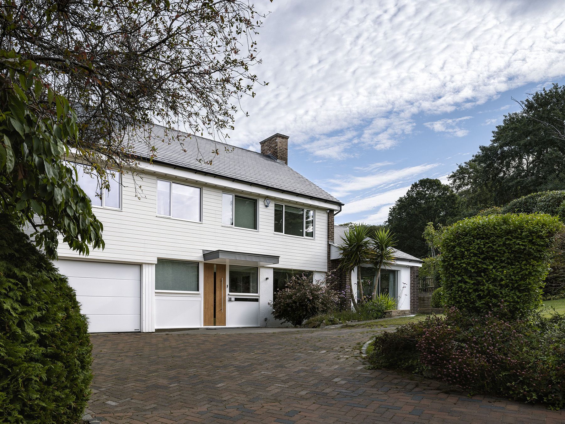 White house with garage, dark roof, and landscaped driveway under a partly cloudy sky.