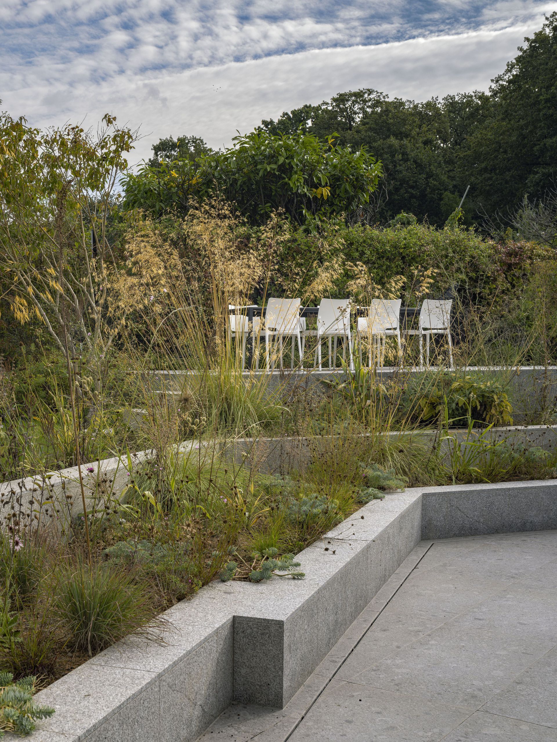 Outdoor garden path with concrete benches, greenery, and signboards under a cloudy sky
