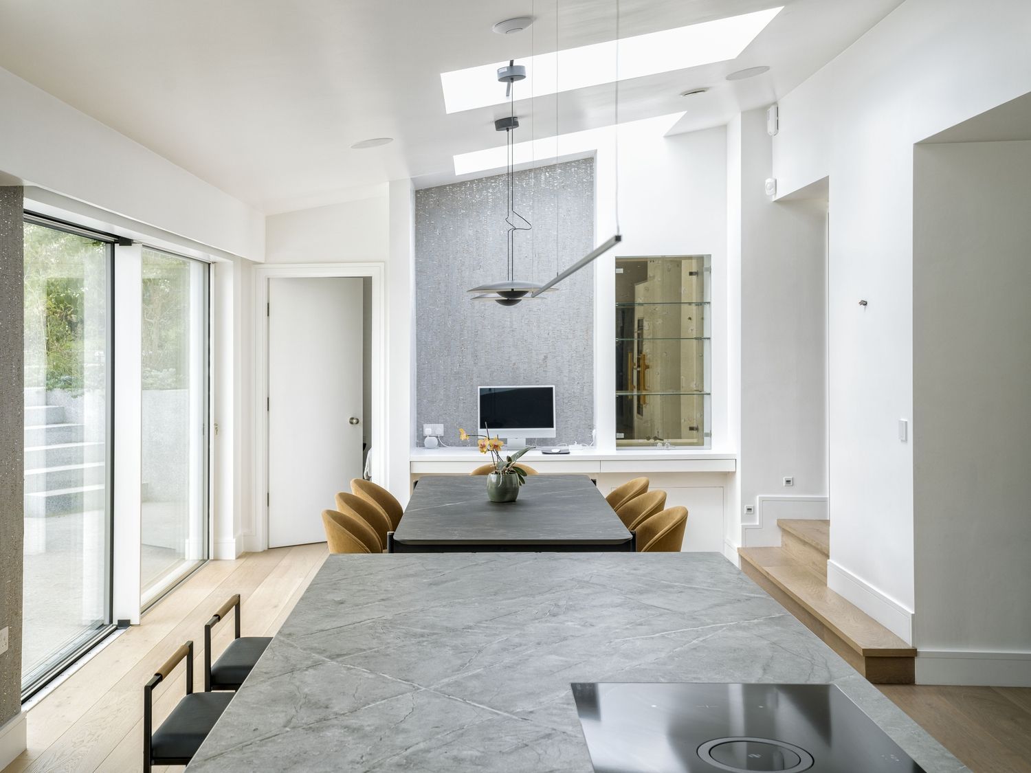 Modern open dining room with a long stone table, gold chairs, and sliding glass doors to a patio