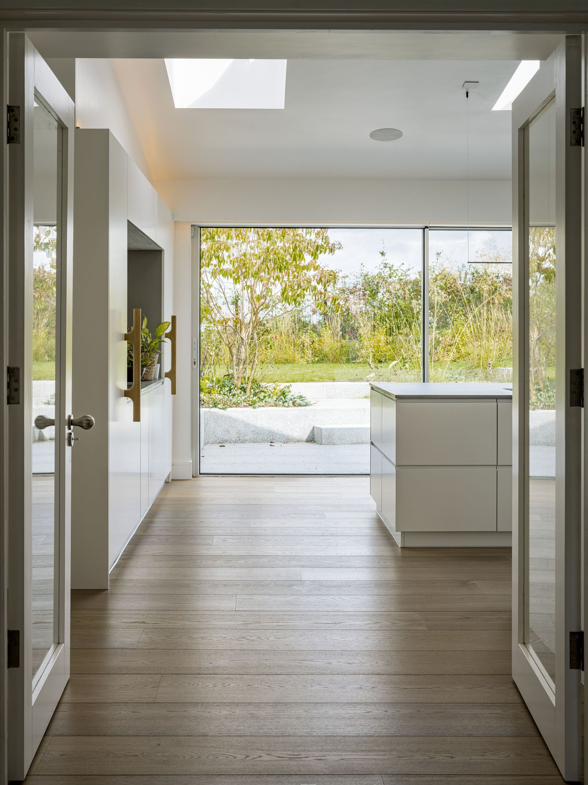 Open doorway to a bright modern interior with wood floors and a view of trees outside