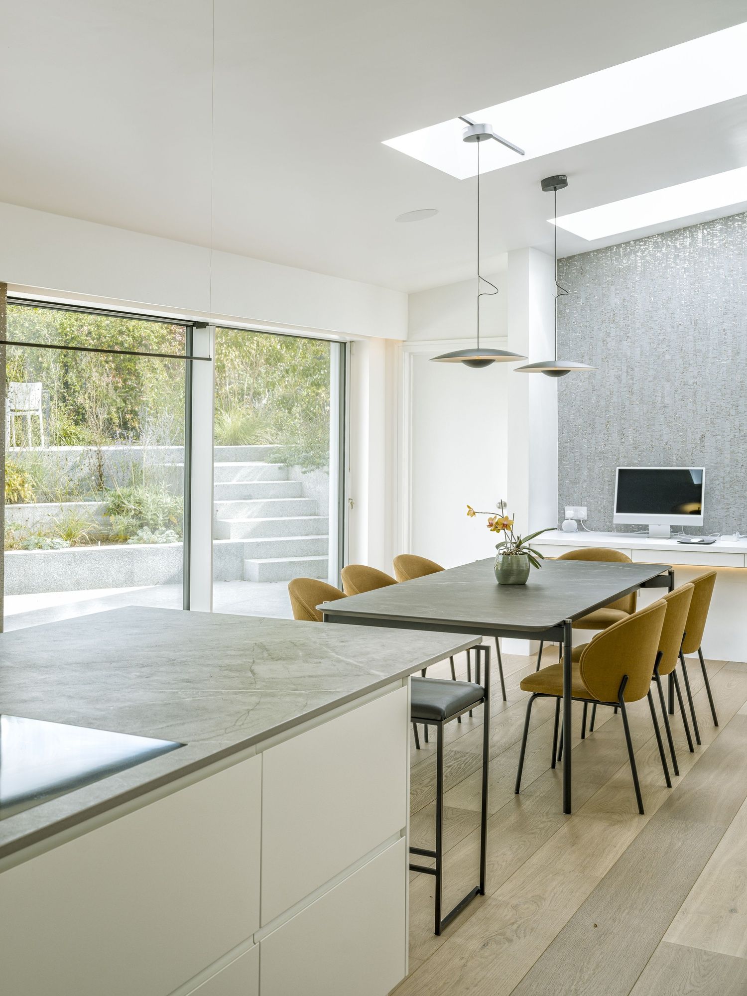 Bright modern kitchen and dining area with white cabinets, wood floor, and mustard chairs by large windows