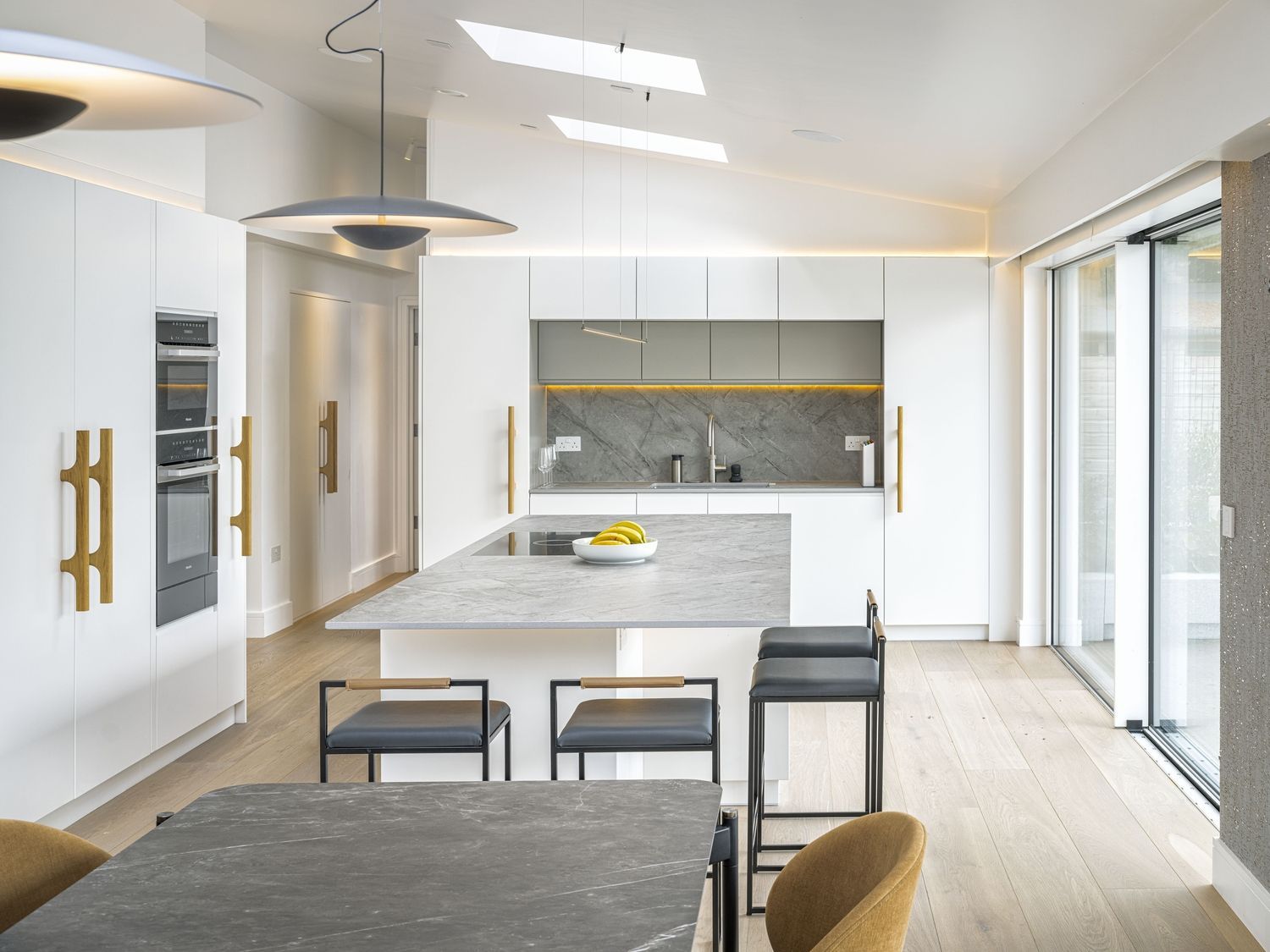 Modern white kitchen and dining area with island, pendant lights, and large sliding glass doors