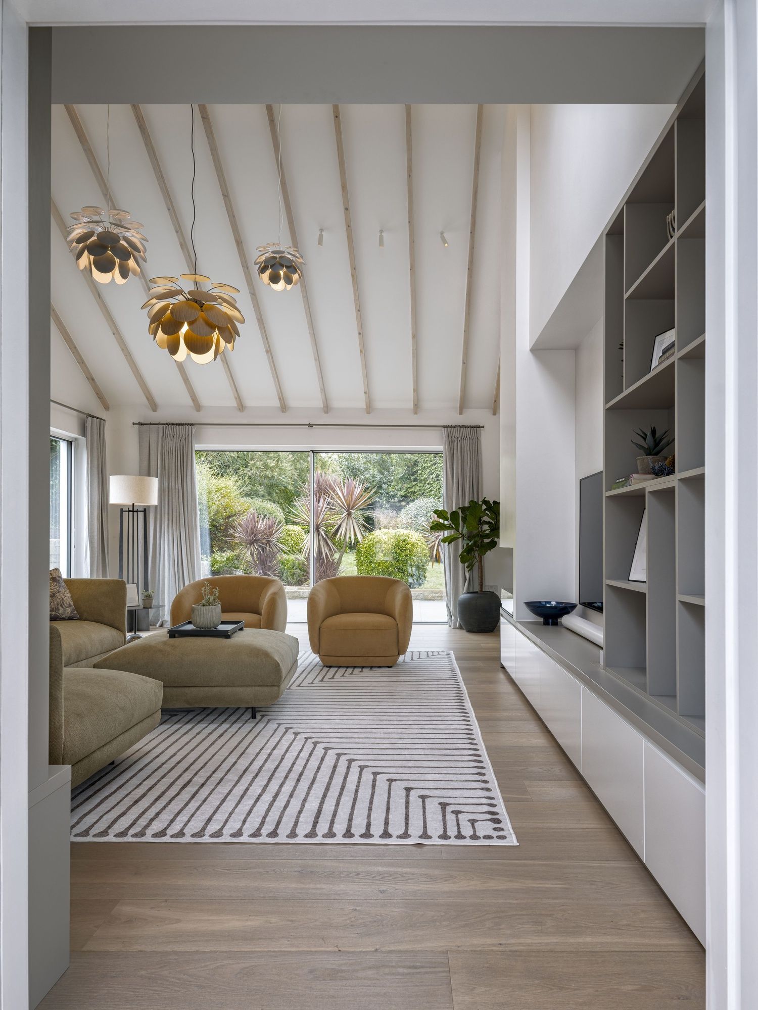 Modern living room with striped rug, light wood floors, gold pendant lights, and open patio doors.