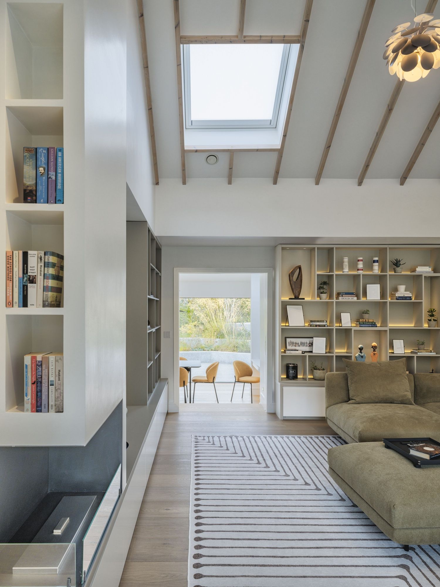 Modern living room with skylight, built-in shelving, striped rug, and mountain view through open doors