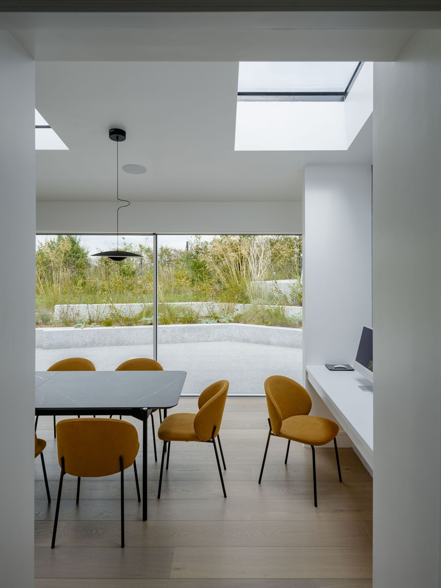 Modern dining room with white table, mustard chairs, and large windows overlooking greenery