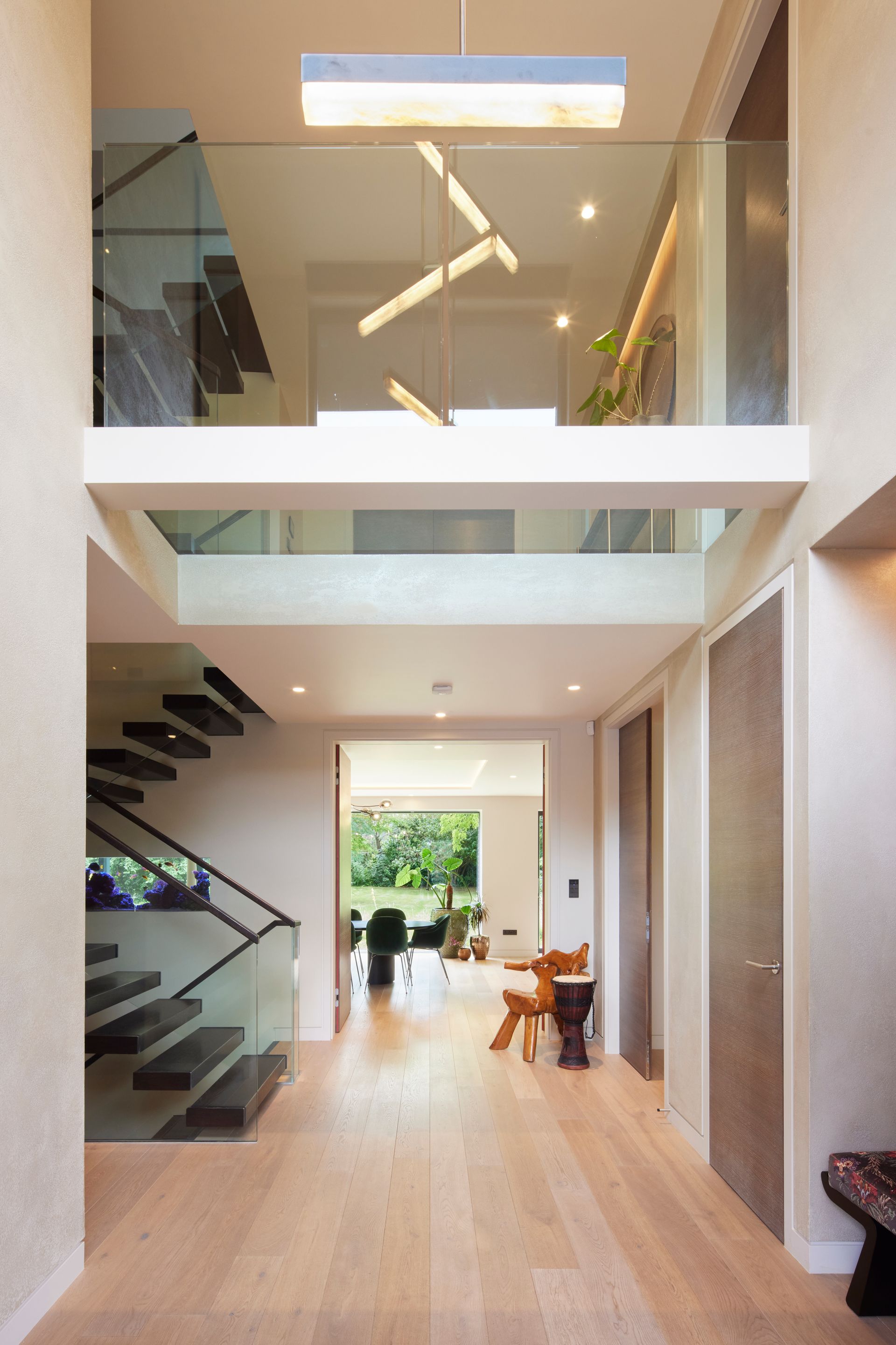 Modern two-story atrium with glass railings, floating stairs, and a bright hallway leading to a garden view