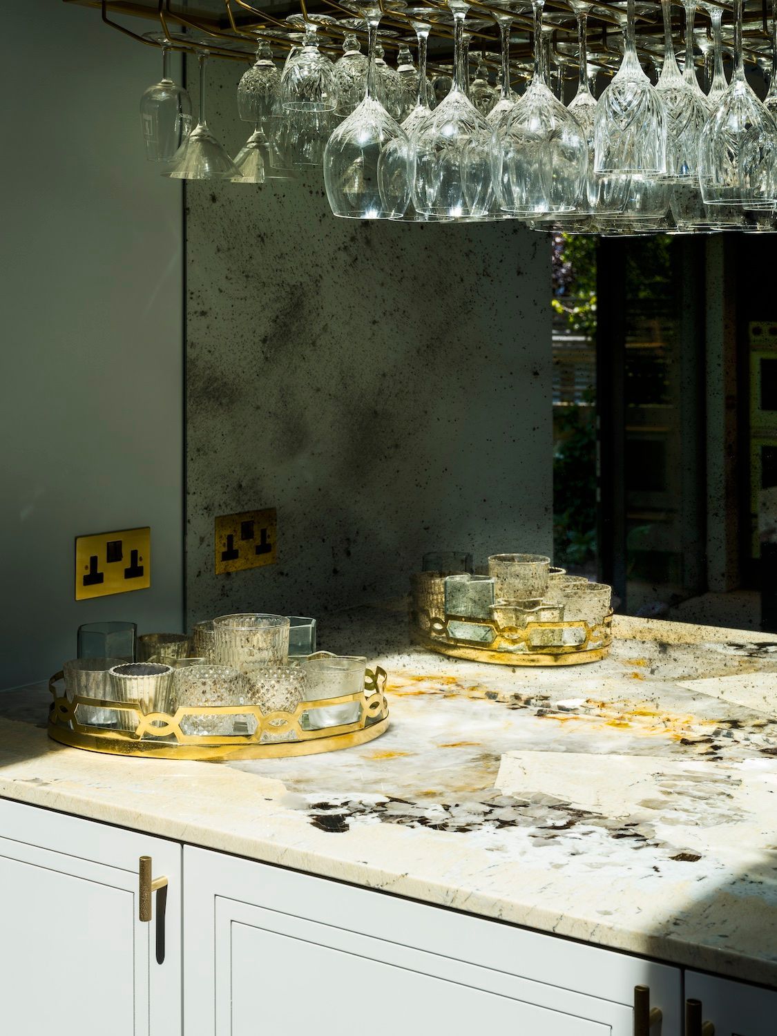 Kitchen counter with broken glassware and spilled debris under hanging wine glasses.