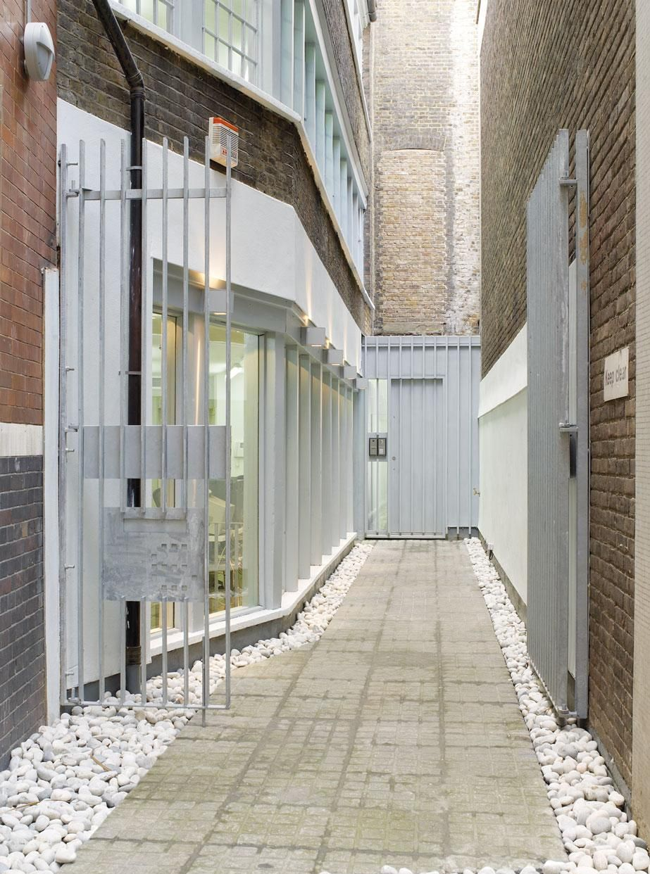 Narrow outdoor walkway between brick buildings, with glass windows and white gravel borders.
