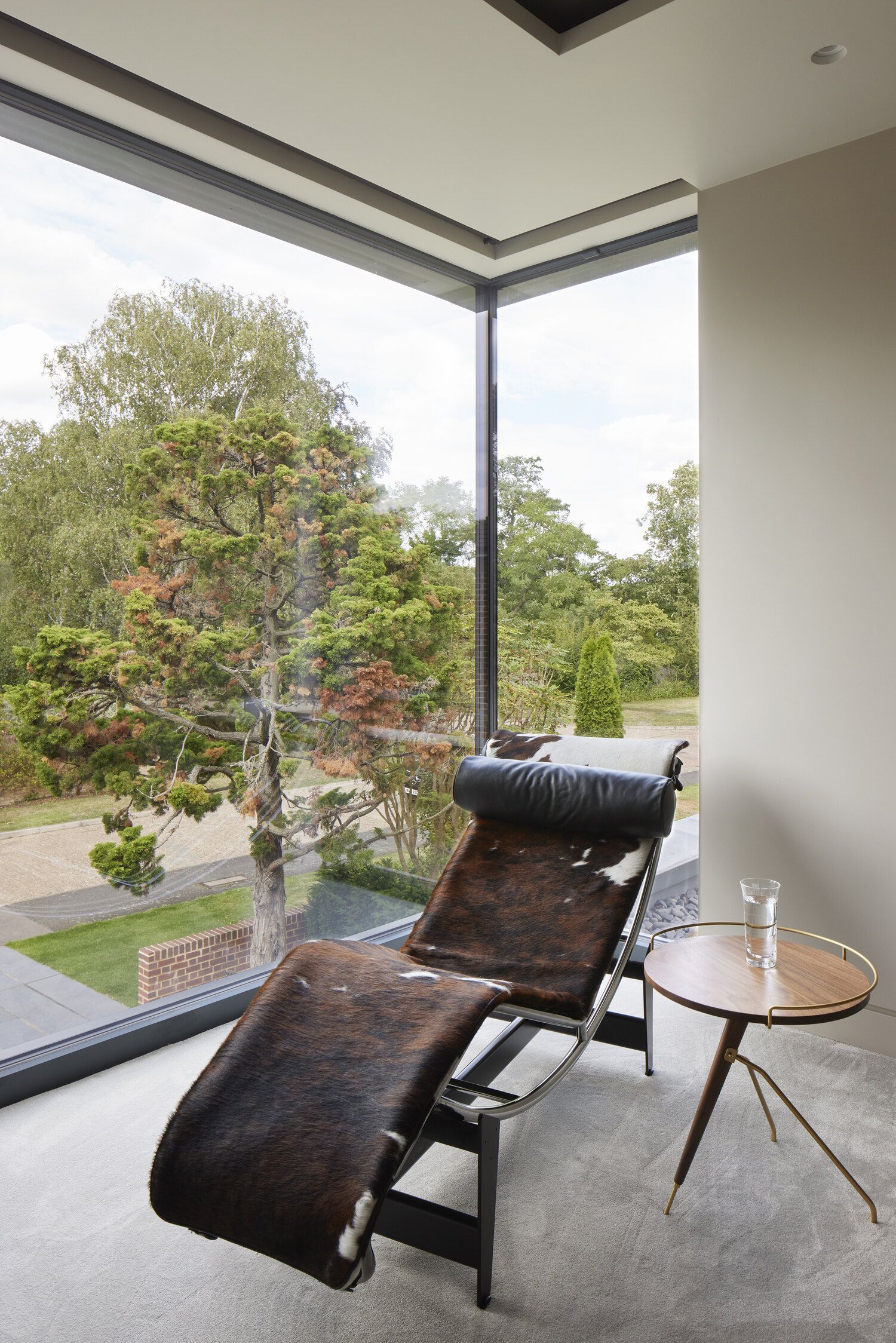 Modern lounge chair by a floor-to-ceiling window overlooking a garden