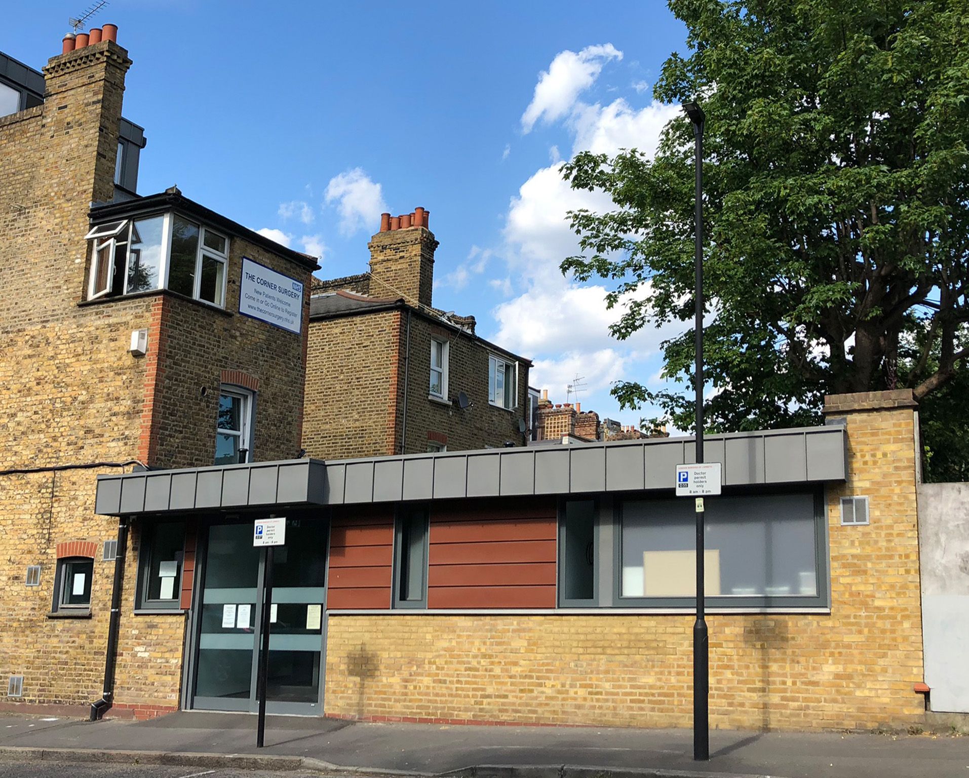 Stone building with a gray storefront, brick wall, and large tree under a blue sky
