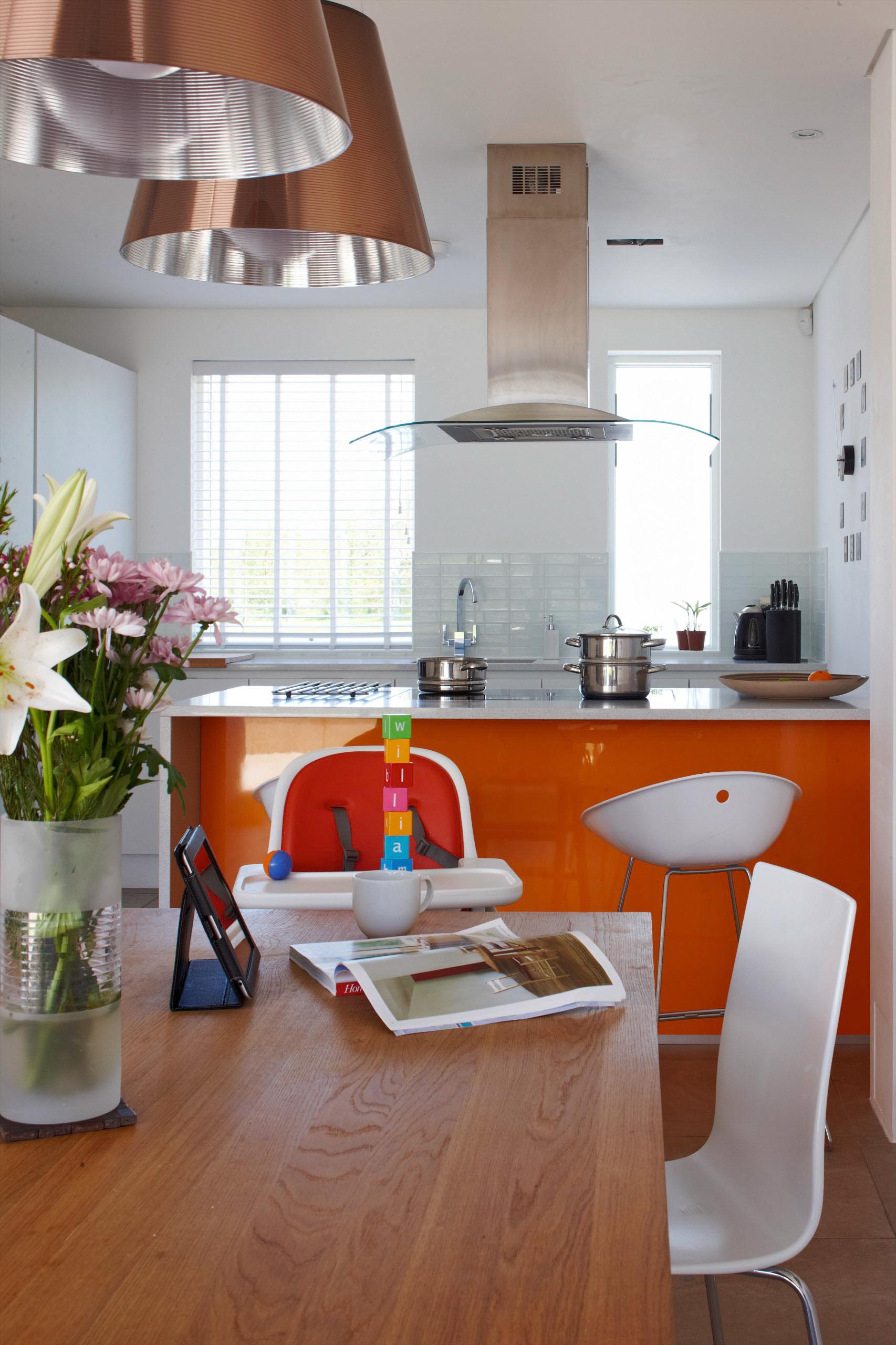 Modern kitchen and dining area with wooden table, orange cabinets, white chairs, and a window