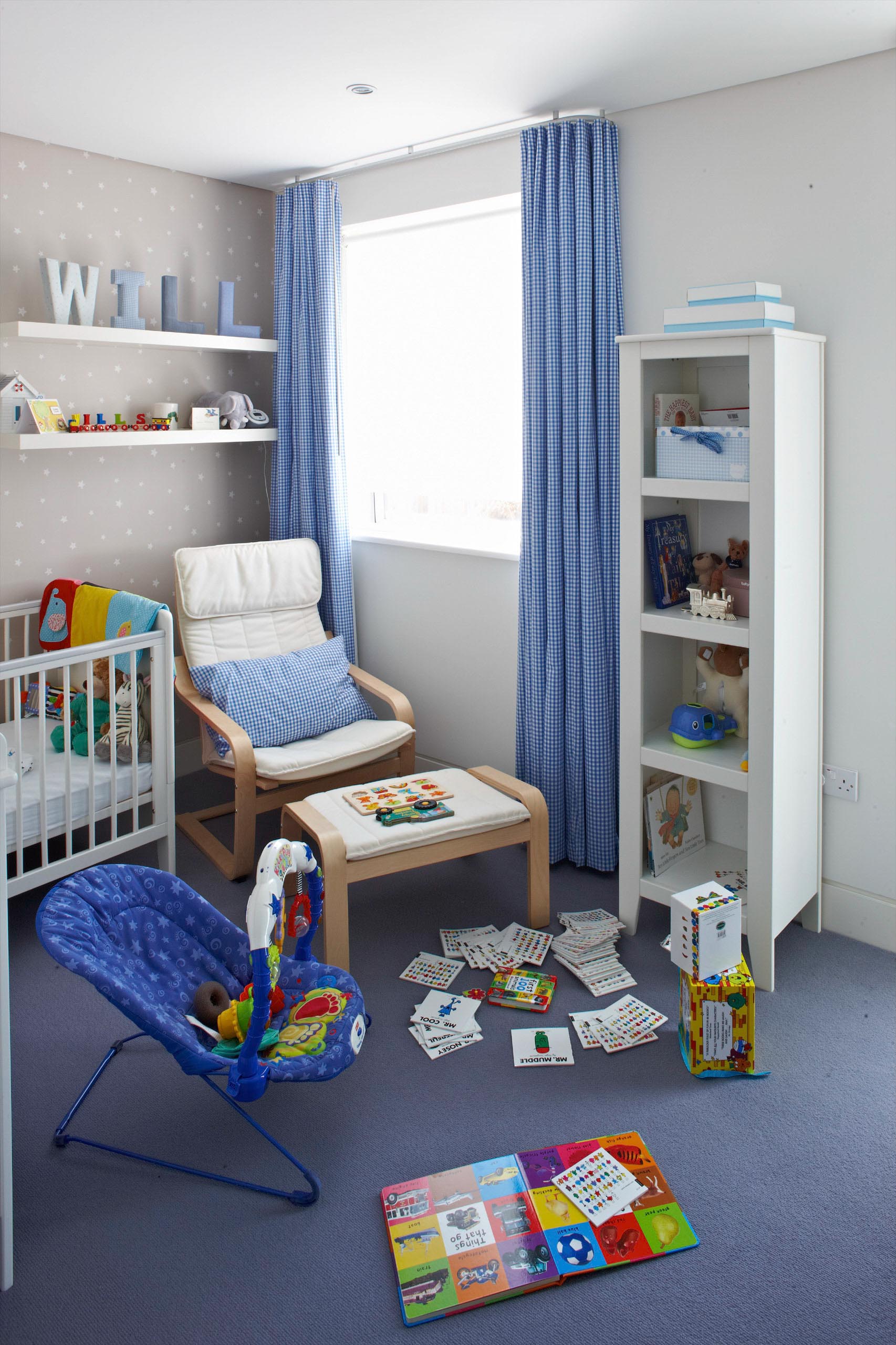Children’s playroom with crib, chair, toy shelf, books, and scattered toys on blue carpet