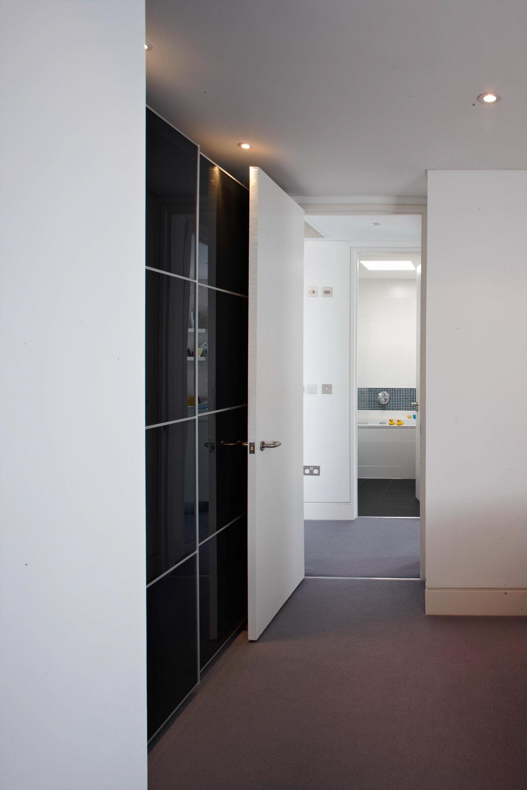 Modern hallway with white walls, carpeted floor, and open doors leading to a bright room.