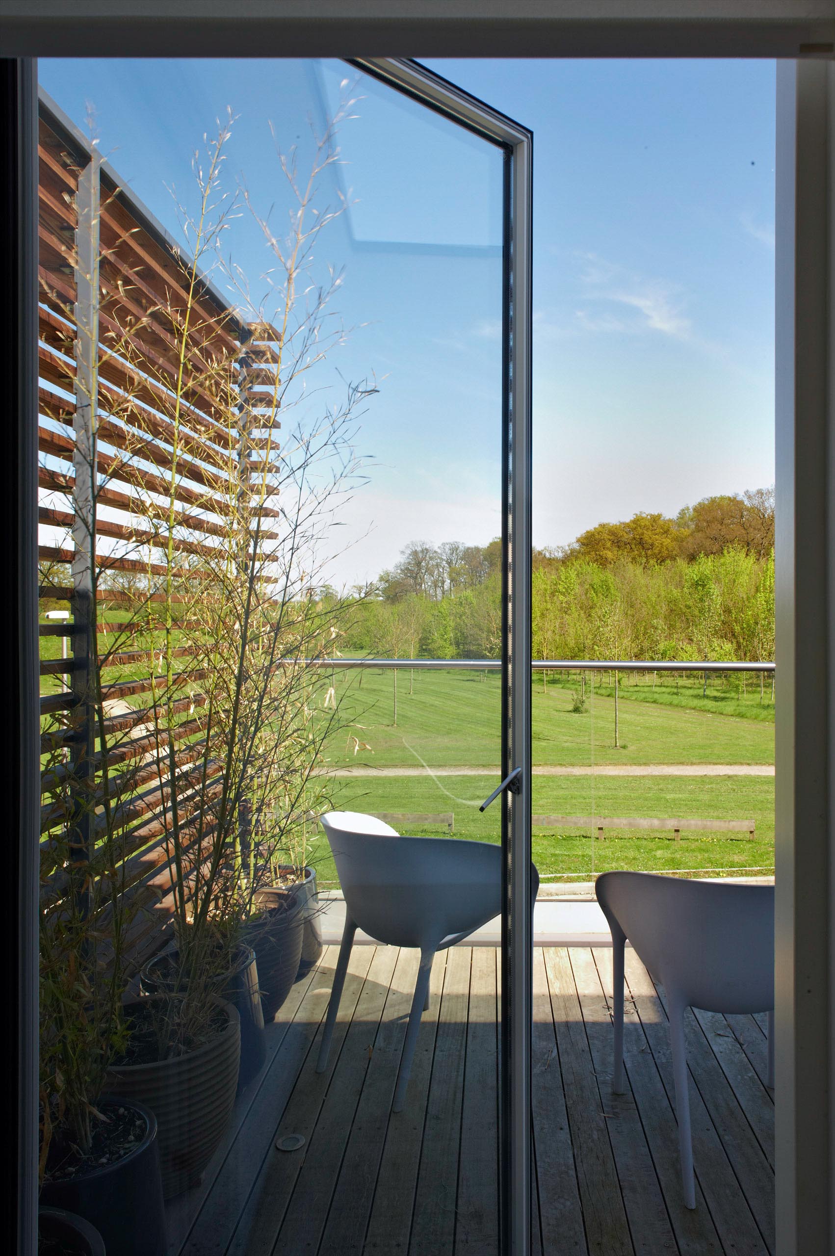 Balcony with white chairs overlooking a green field and blue sky through a glass door