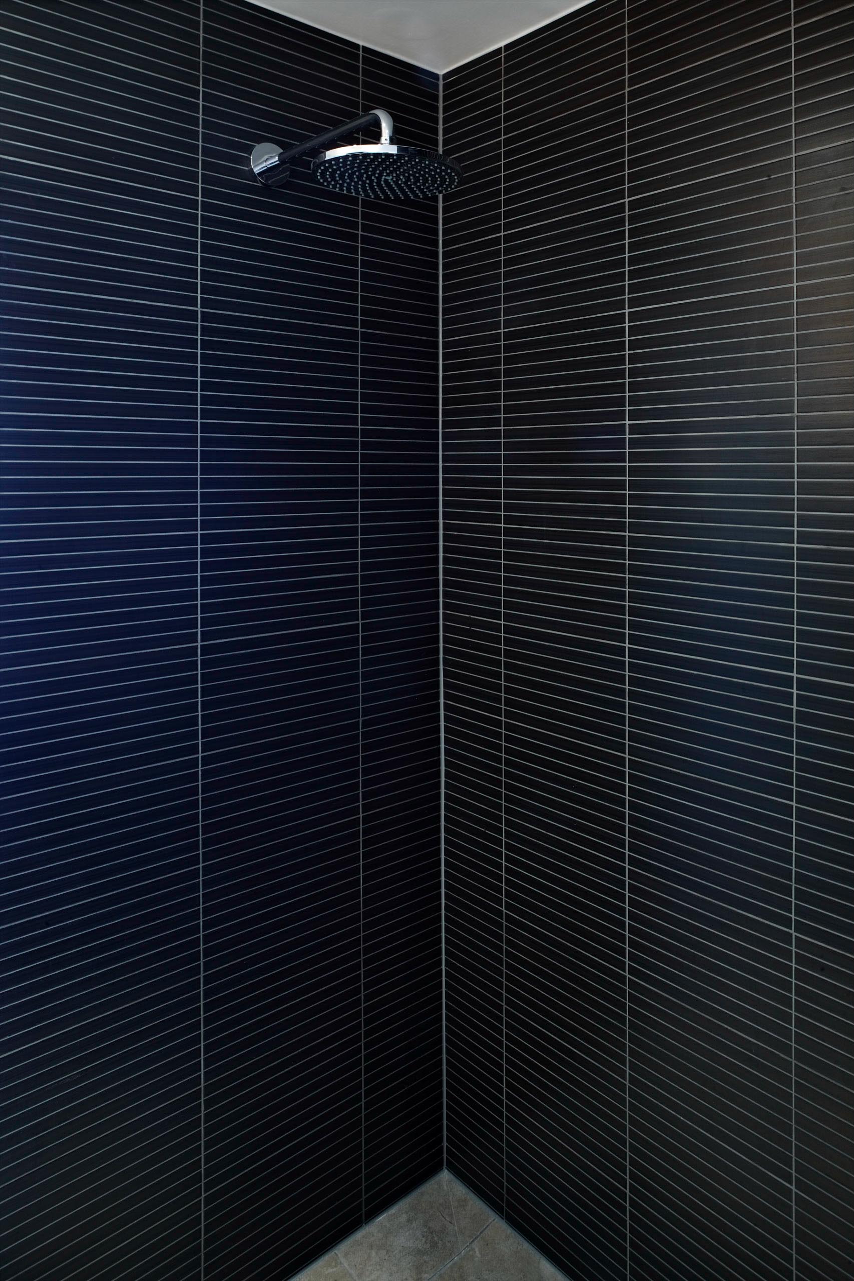 Dark shower stall with black patterned walls and a silver showerhead.
