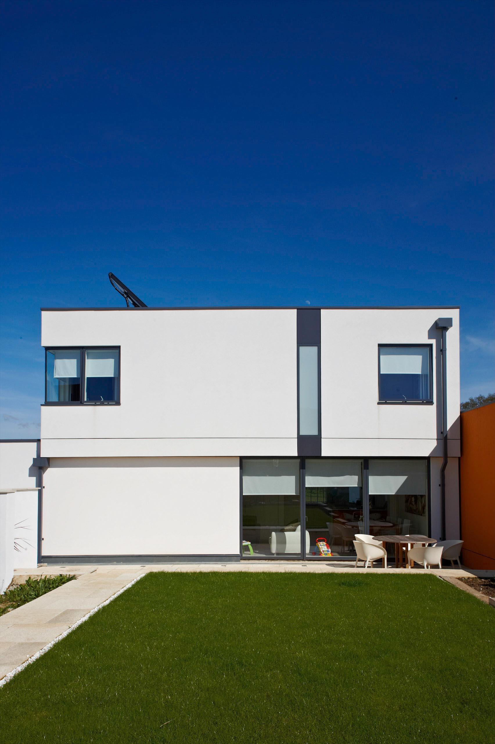 Modern white two-story house with large windows and a green lawn under a clear blue sky