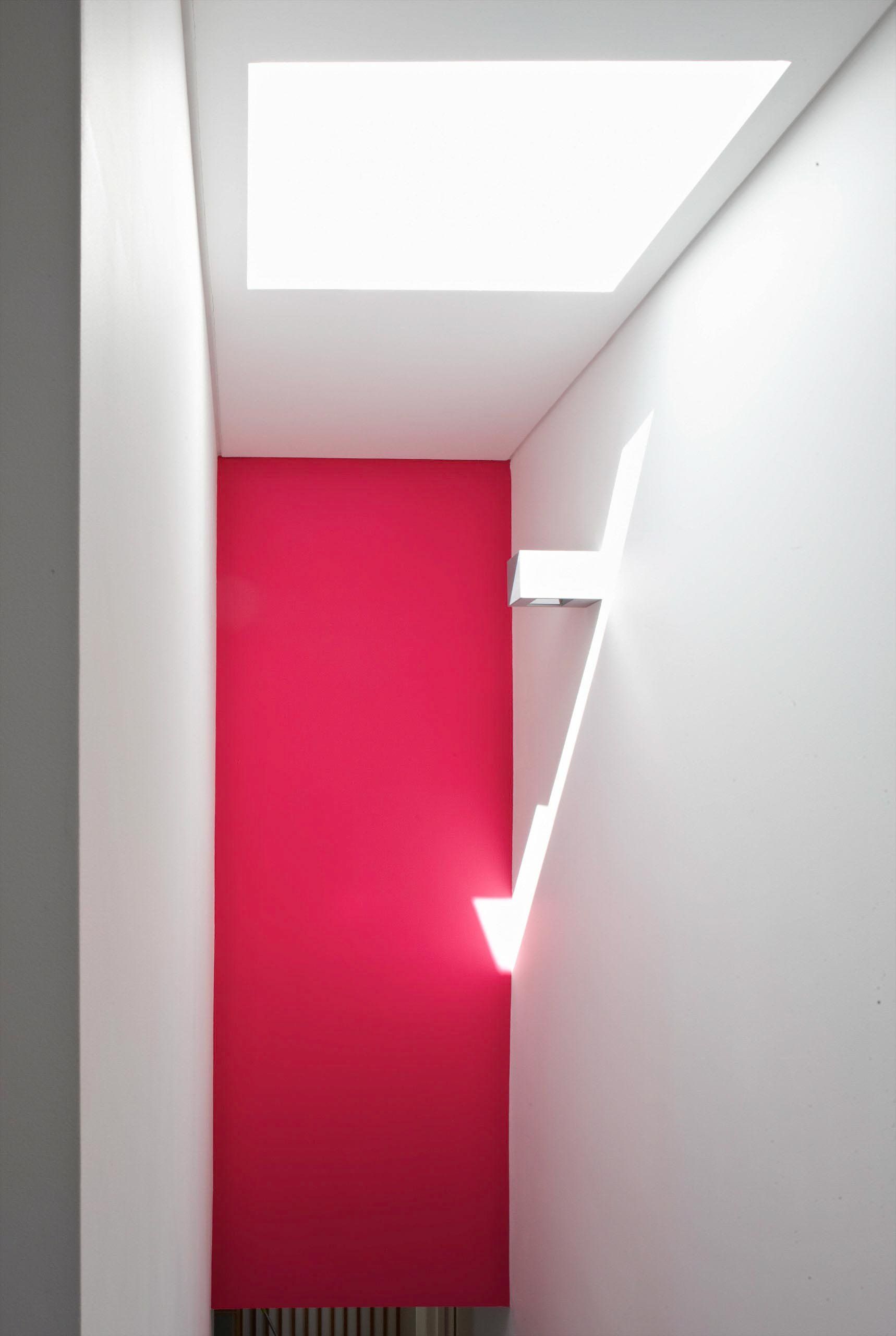 Narrow white hallway with a bright pink wall at the end and a skylight above