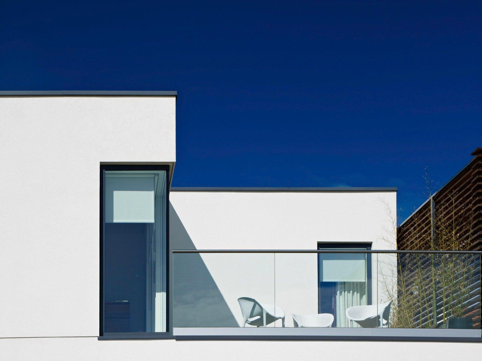 Modern white building with blue windows and a rooftop terrace under a clear blue sky