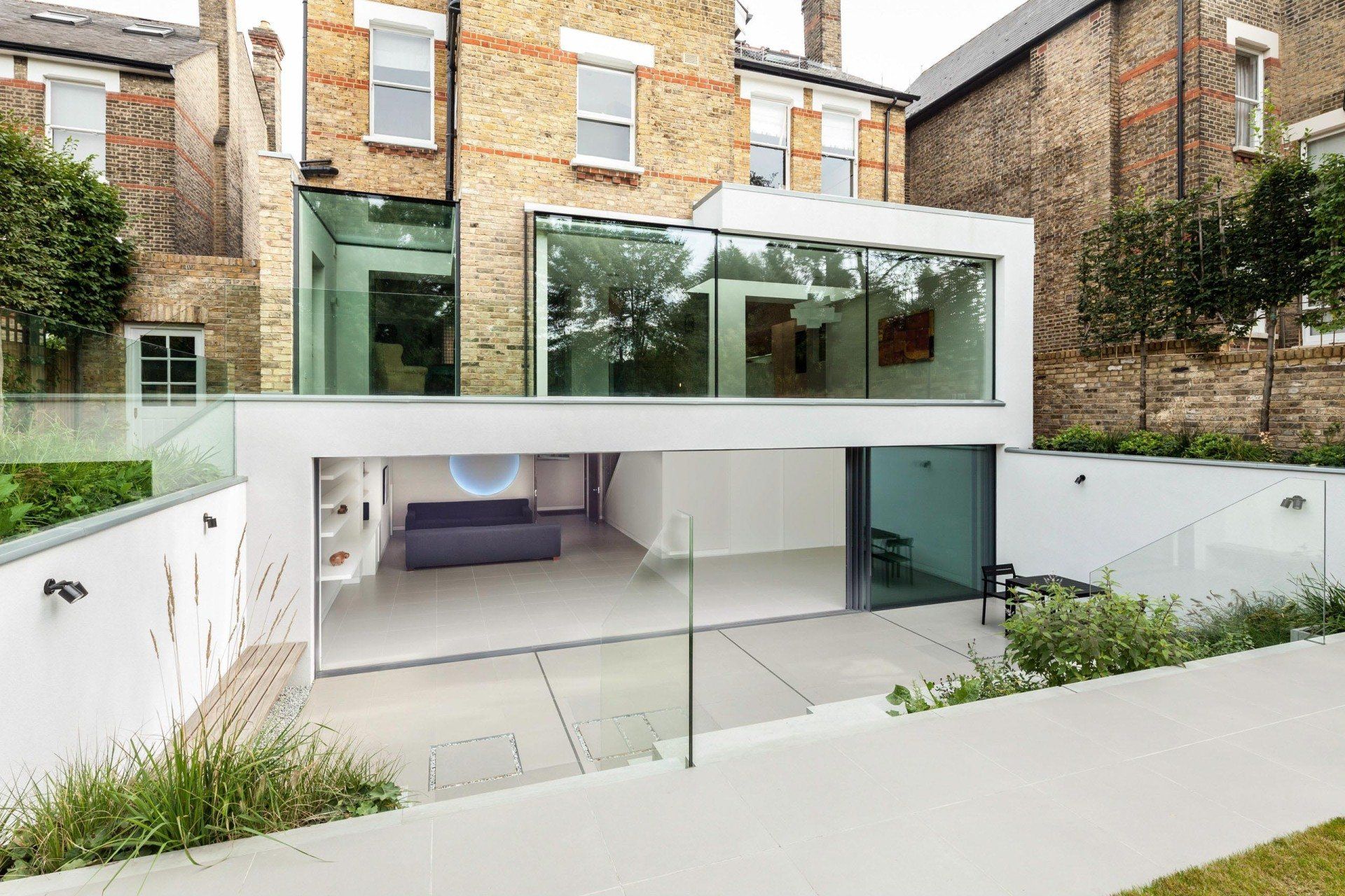Modern white-and-glass home extension with patio and garden, viewed from the back yard