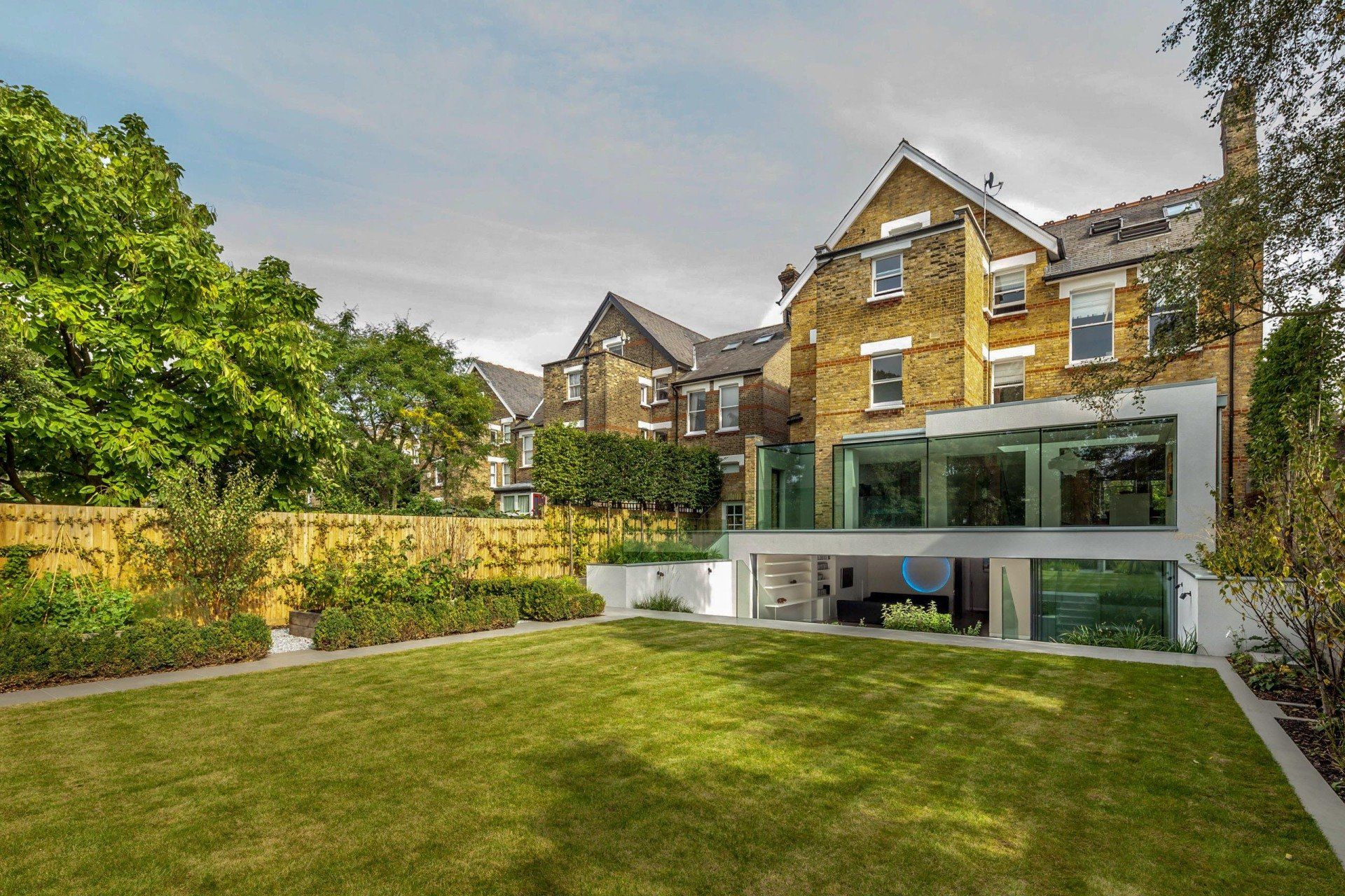 Backyard lawn with modern glass extension behind a stone townhouse and garden trees