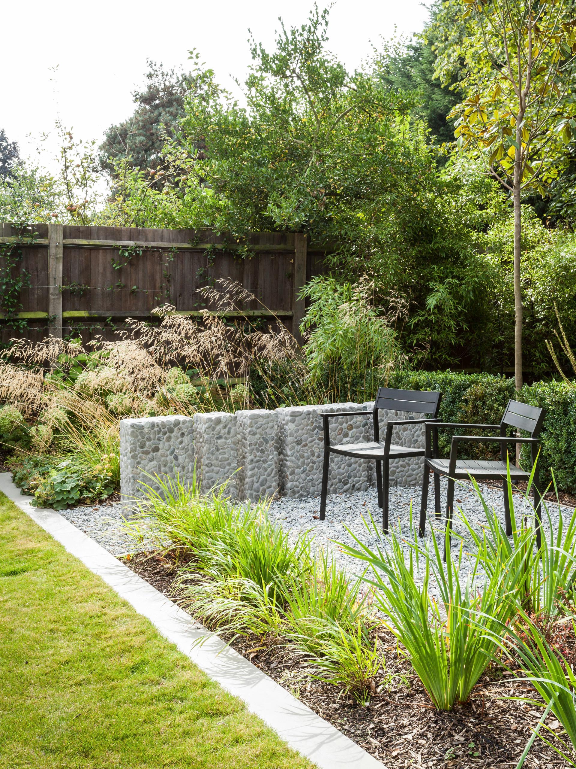 Backyard patio with gravel seating area, black chairs, and lush green plants