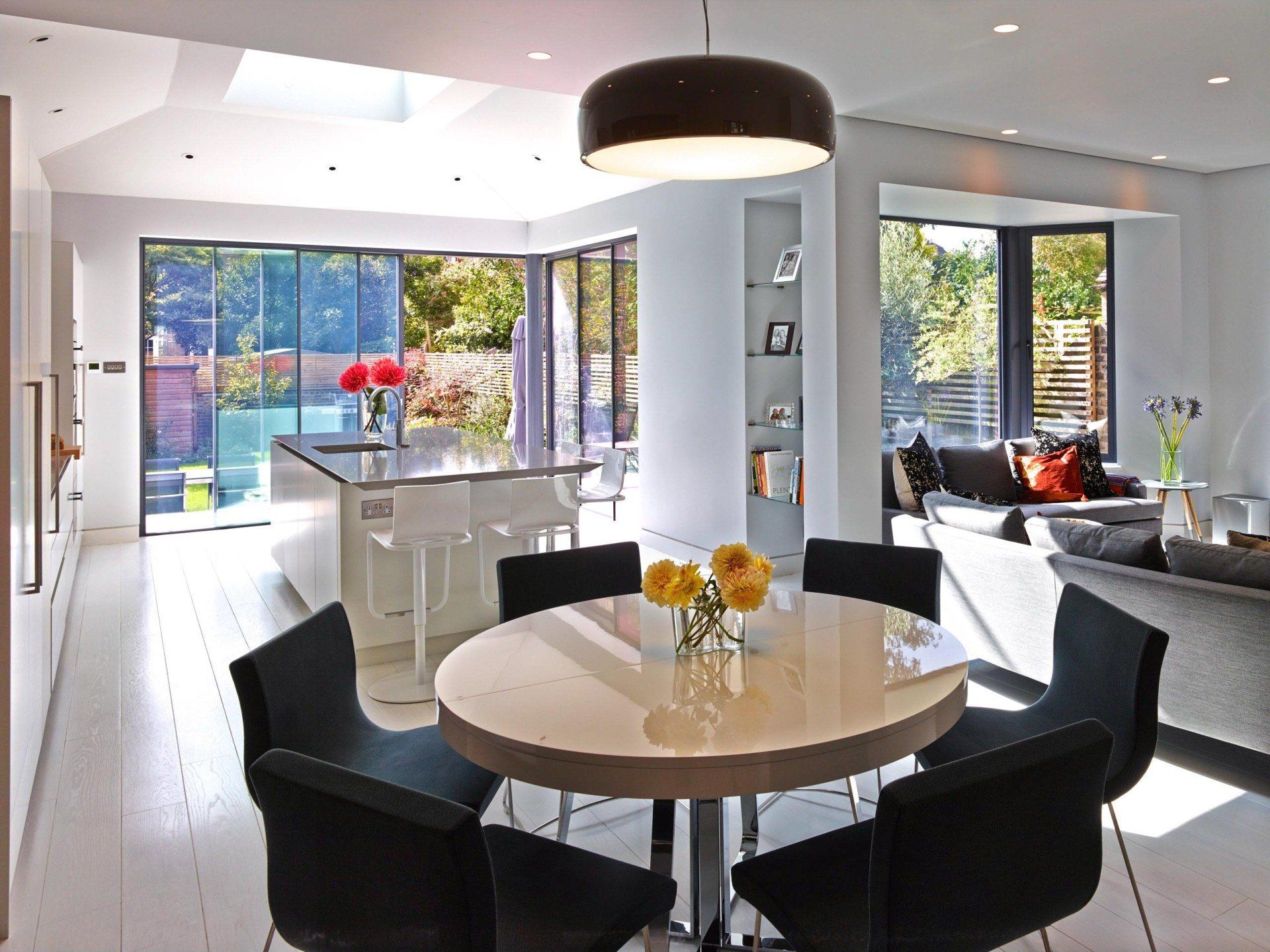 Modern kitchen and dining area with round table, black chairs, and large windows.