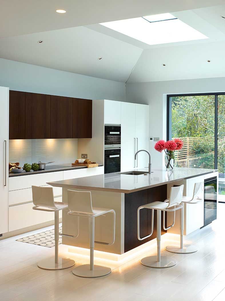 Modern white kitchen with island, pendant lights, dark cabinets, and large windows overlooking greenery
