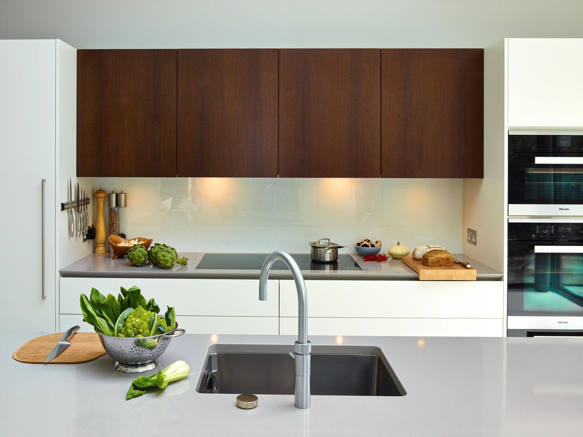 Modern kitchen with wood cabinets, white countertops, a sink island, and fresh vegetables on the counter