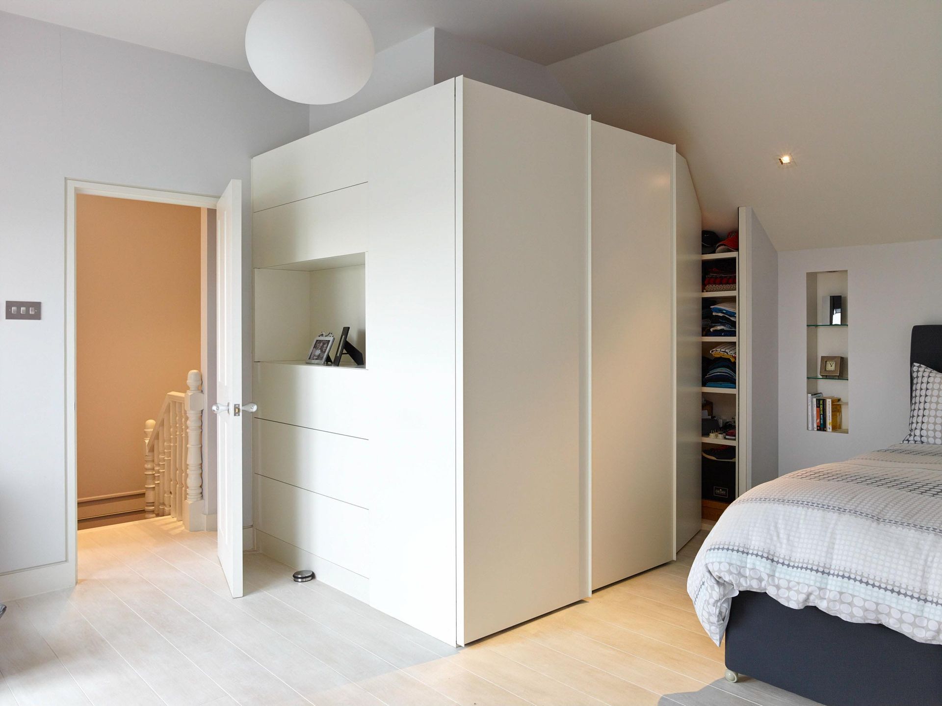 Modern bedroom with white wardrobe, open bathroom door, and gray bed in soft natural light