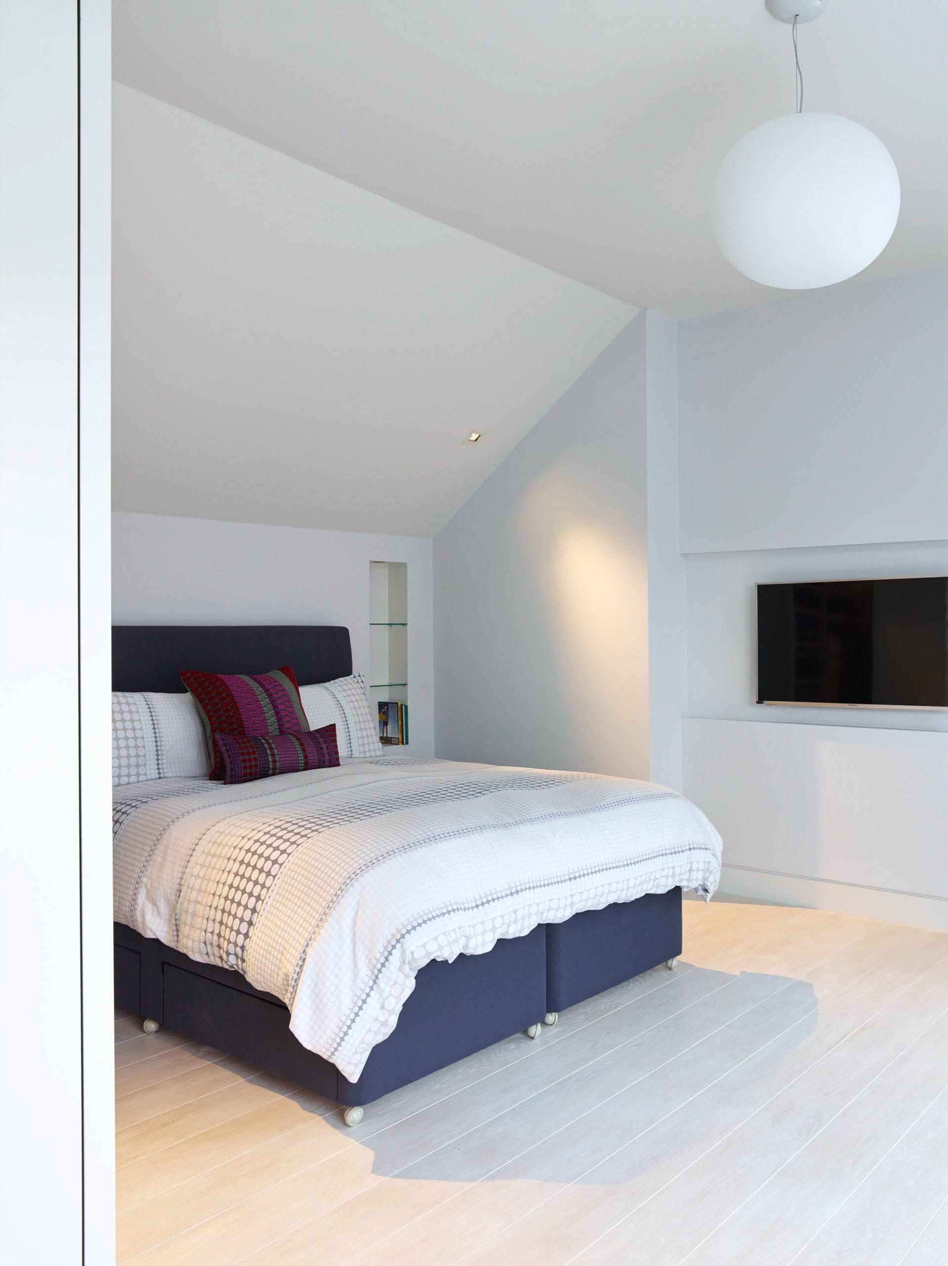 White bedroom with a navy blue bed, white bedding, and a TV on the wall.