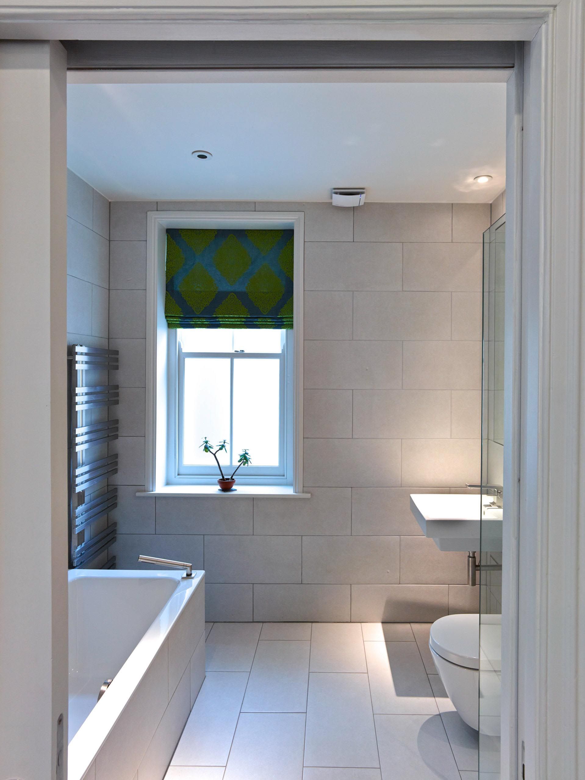 Bright modern bathroom with a bathtub, window, sink, and white tiled walls