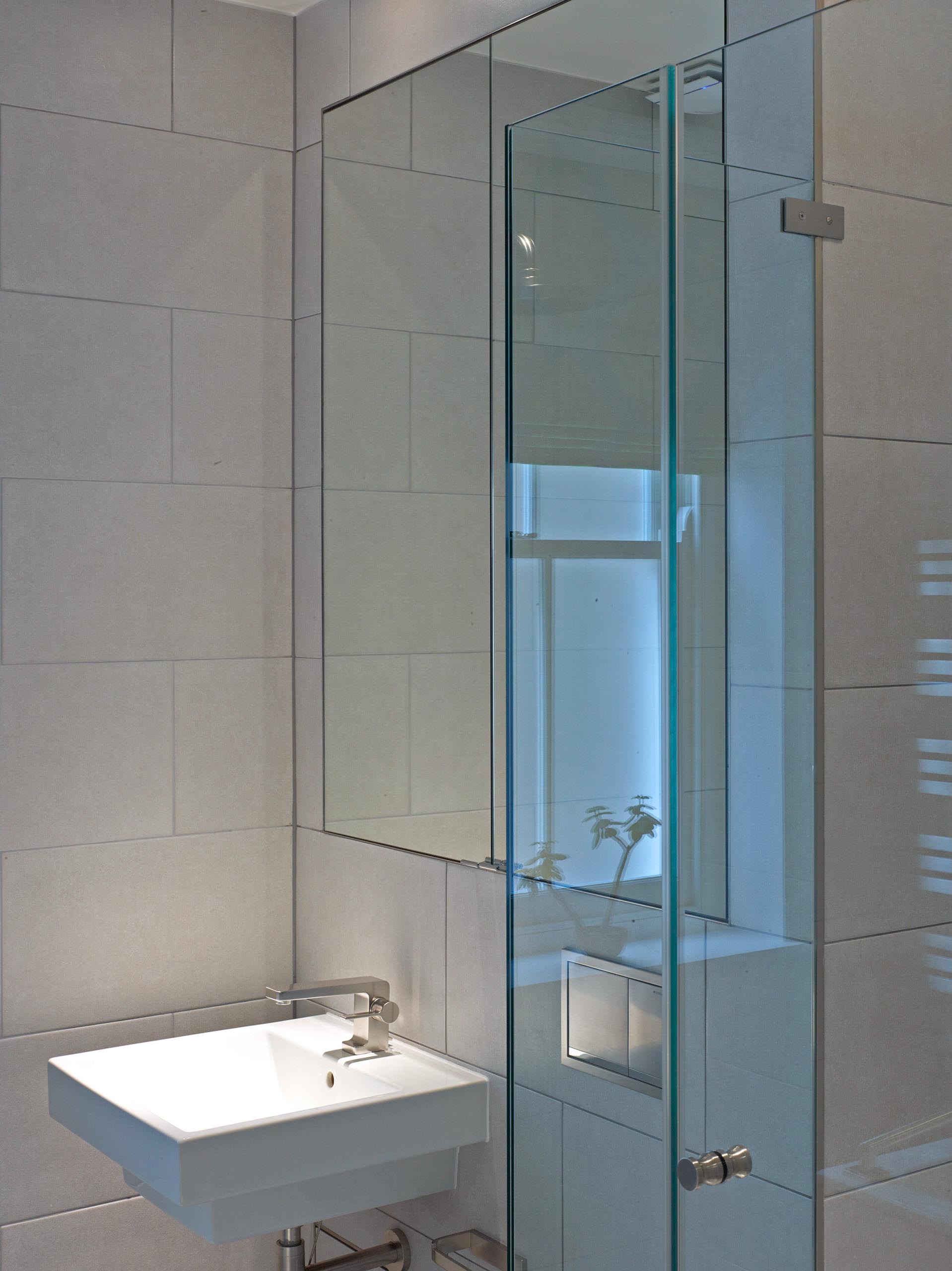 Modern bathroom with white sink, glass shower, and mirrored cabinet on white tiled walls.