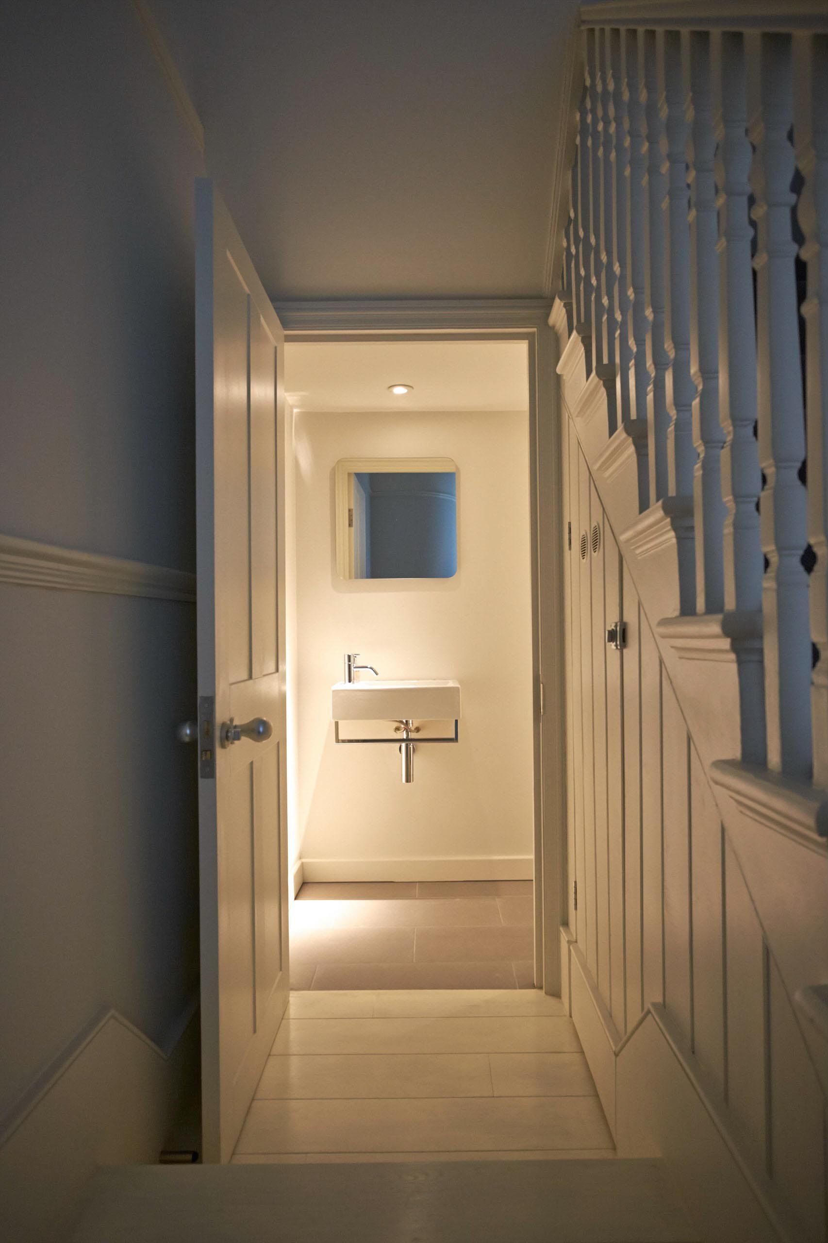 Hallway with doorway leading to a small bathroom. White walls, stairs on right, and a sink/mirror in the doorway.