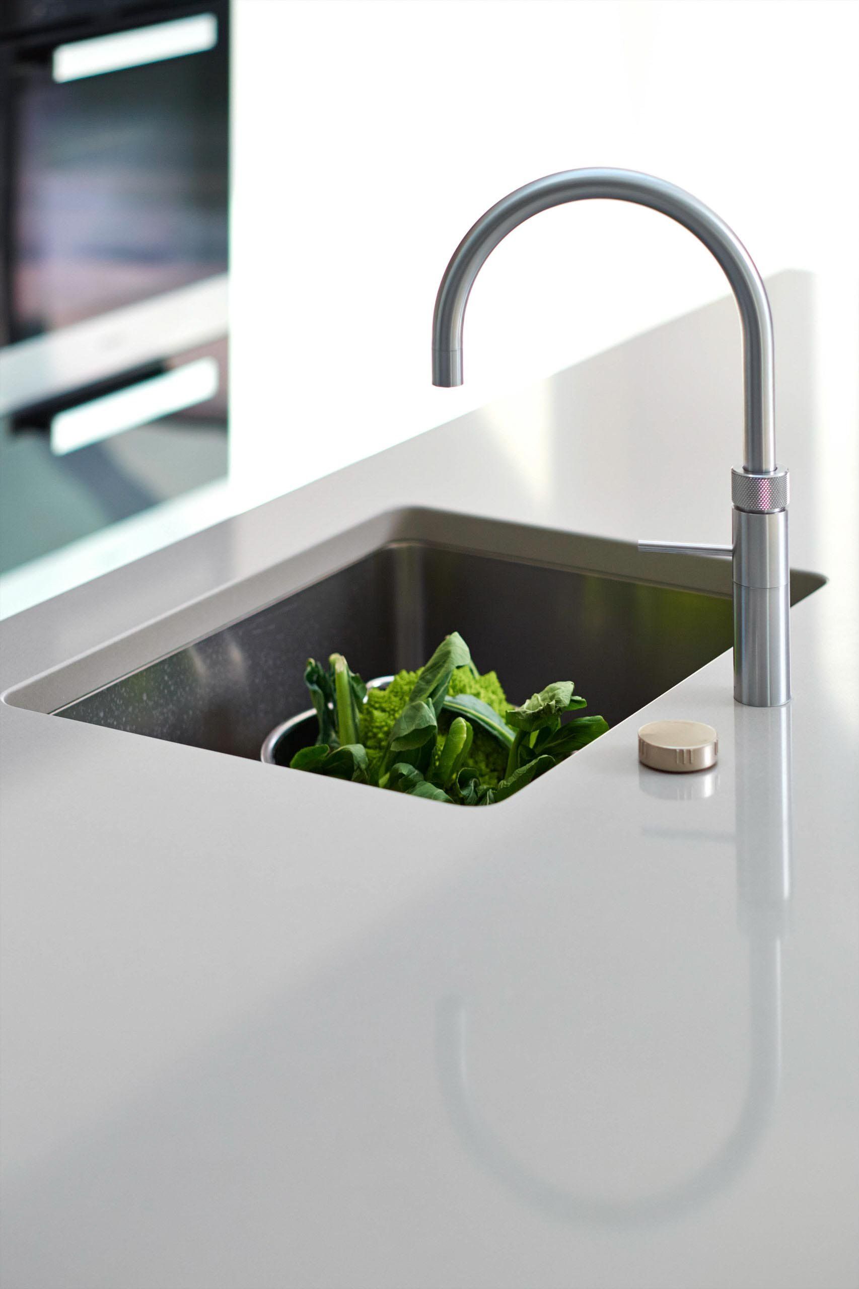 Stainless steel kitchen sink with greens, modern faucet, and light countertop.