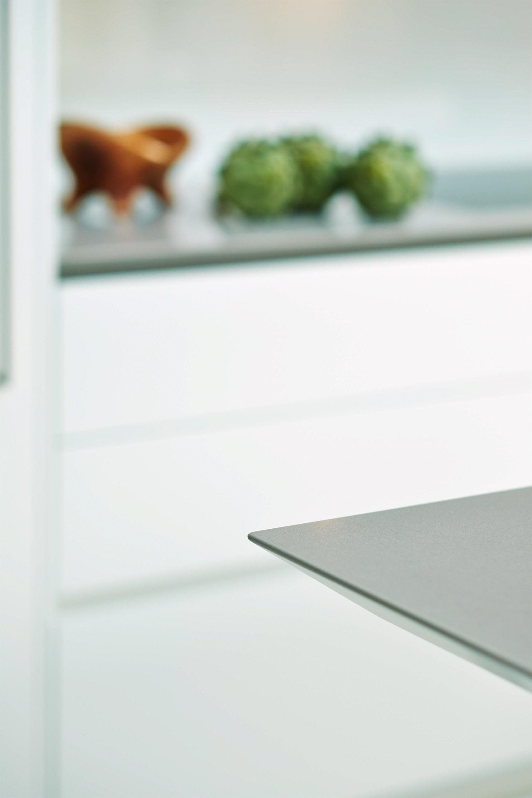 Close-up of a silver counter edge with a blurry view of white cabinets and artichokes.