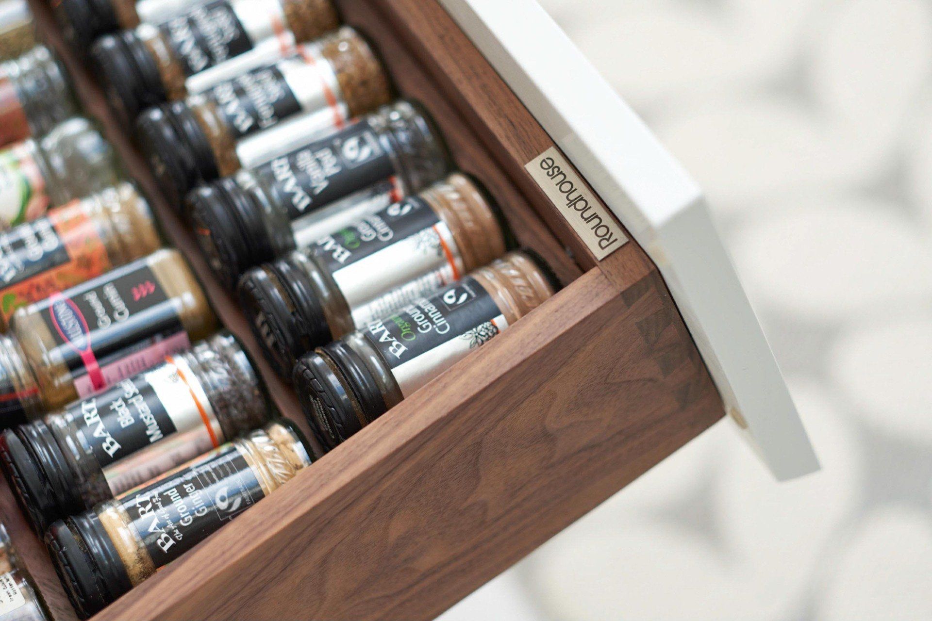 Spice drawer filled with labeled spice jars, inside a brown wooden drawer with a white edge.