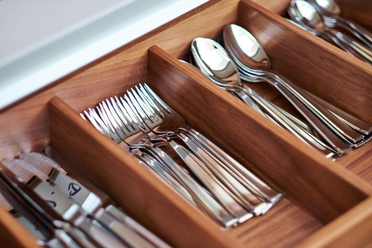Wooden drawer with silverware organized in compartments.