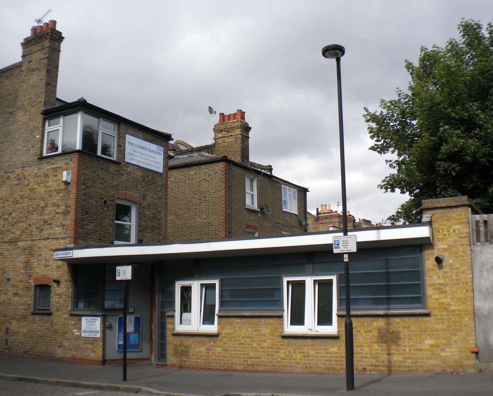 A brick train station building with a low blue-gray entrance and a tall chimney beside a streetlamp.