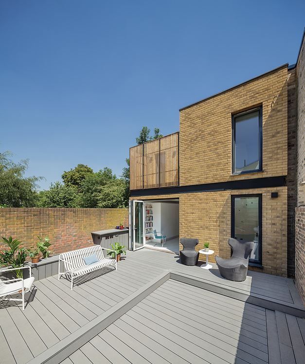 Modern brick house with large gray deck, outdoor seating, and glass doors under a clear blue sky